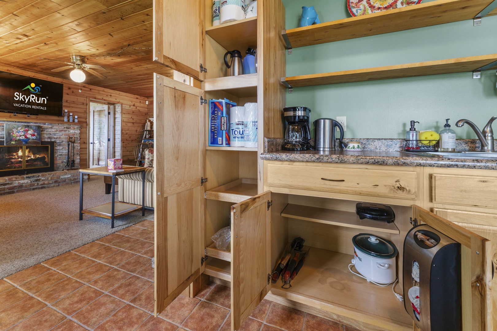 Your fully equipped kitchen features granite counters, coffee maker, and thoughtful storage. Through the open layout, spot the cozy fireplace that invites you to unwind after mountain adventures.