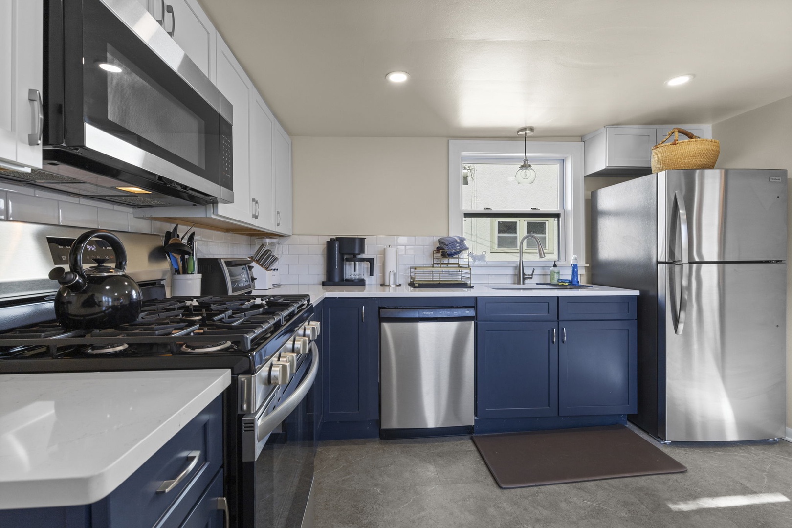 Full kitchen view featuring navy lower cabinets, white uppers, quartz countertops, stainless refrigerator, and dishwasher — stylish and fully stocked.