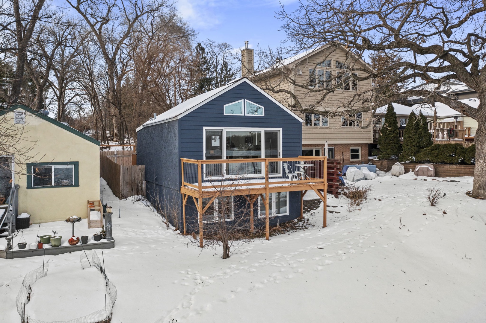 A charming blue cottage with elevated deck nestled in a peaceful winter neighborhood setting.