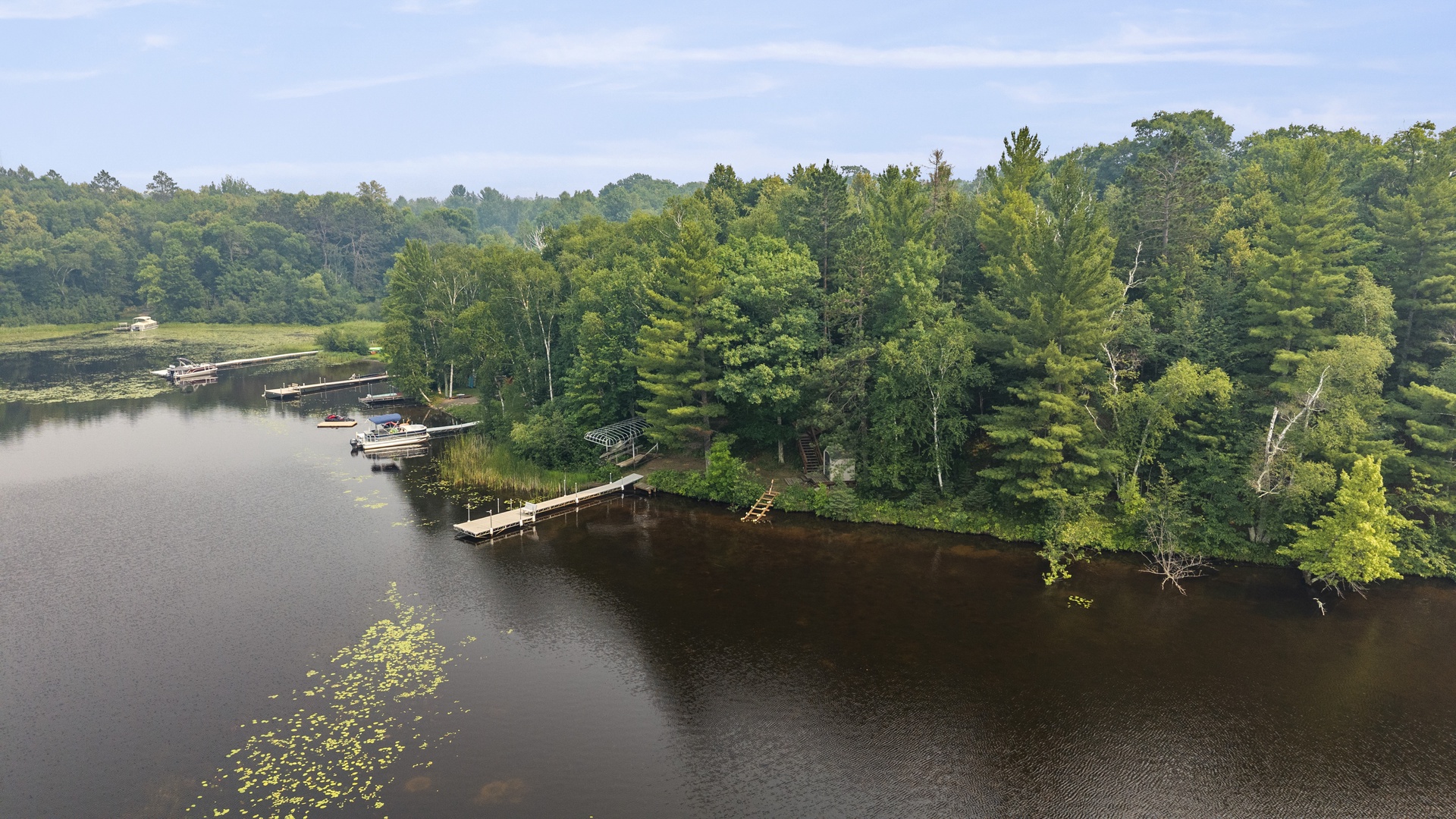 Aerial view of the property's private lakefront setting, featuring a dock with boat access nestled among lush forest and tranquil waters—an ideal natural retreat for outdoor enthusiasts.