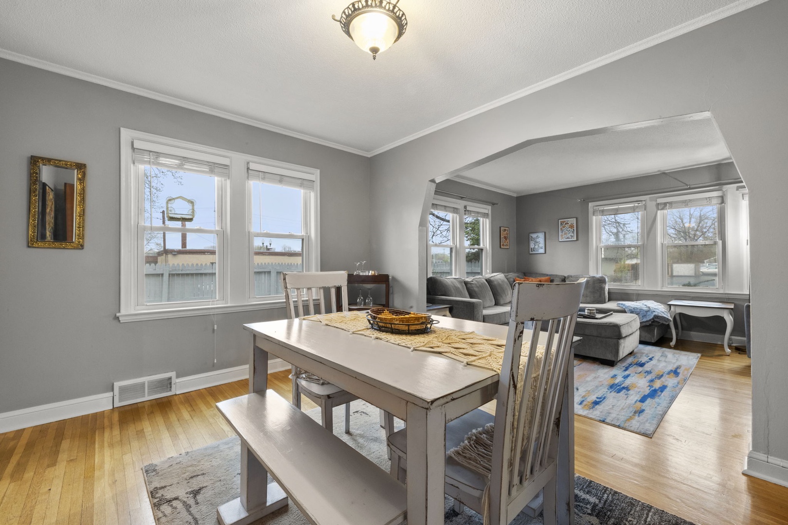Step into your bright, open living and dining space where natural light streams through large windows, hardwood floors warm the room, and cozy seating invites you to unwind after a day of exploring.