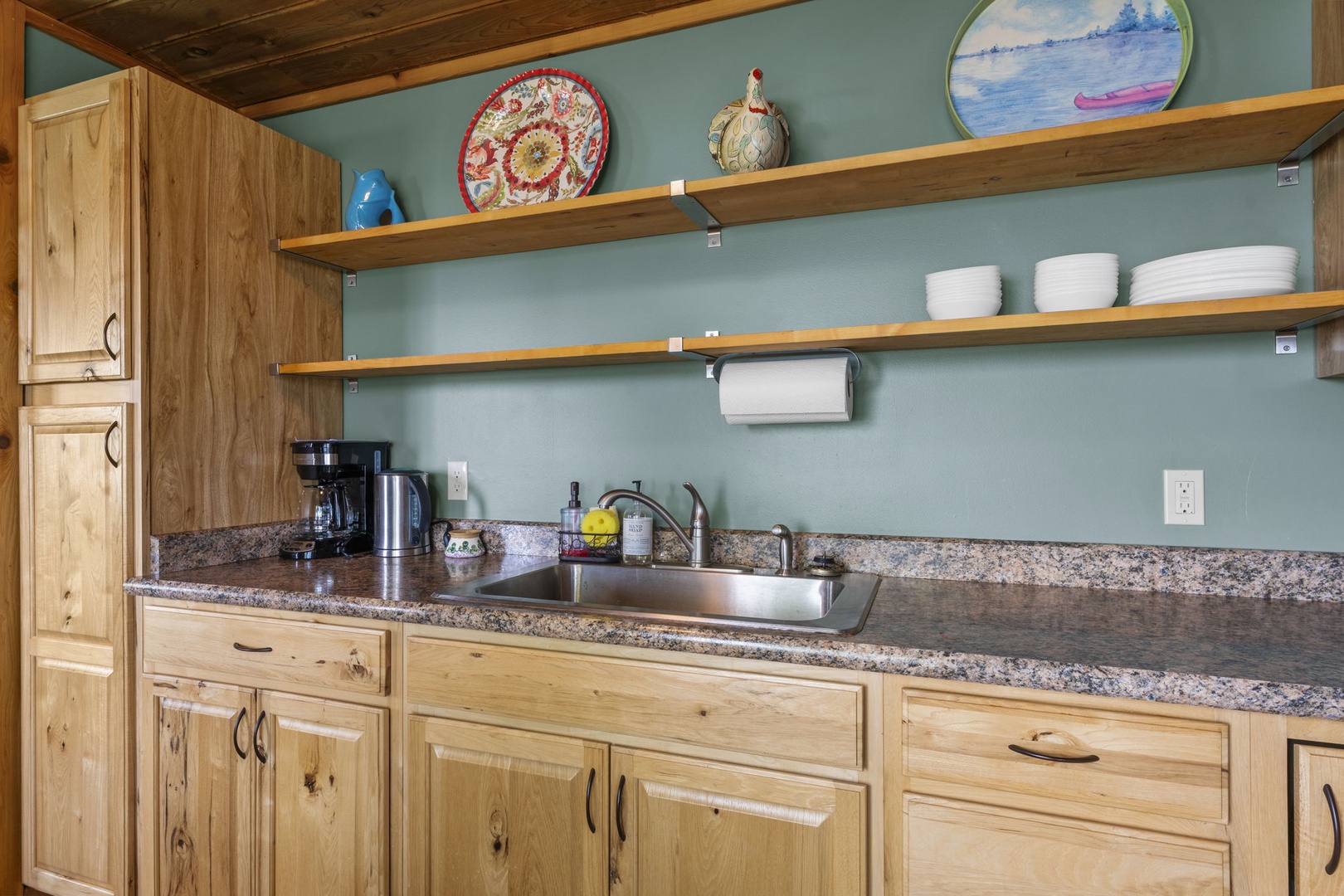 Step into your fully-equipped kitchen with warm wooden cabinetry, granite counters, and open shelving stocked with dishes—ready for your home-cooked meals and morning coffee rituals.