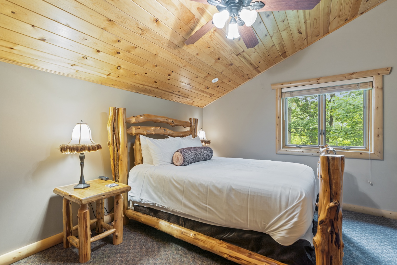 Relax in this cozy bedroom with handcrafted log furniture and vaulted wood ceilings. Your window opens to peaceful forest views, creating a serene mountain retreat.