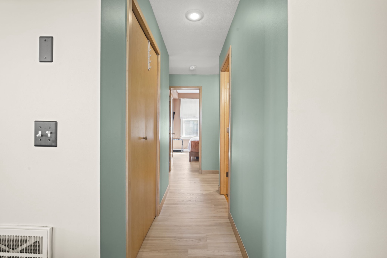 A soothing hallway with soft sage-green walls and warm wood tones welcomes you, leading to your private spaces within the rental.