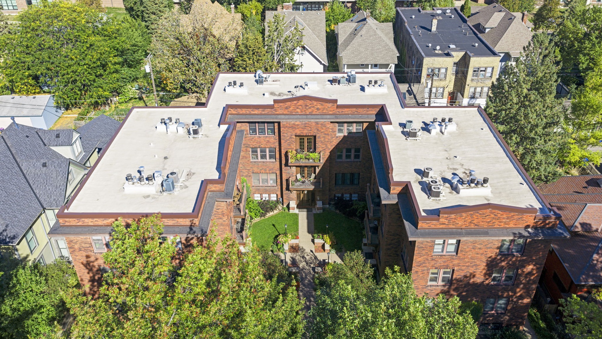 Aerial view of a classic red brick building nestled among tree-lined streets in a charming residential neighborhood.