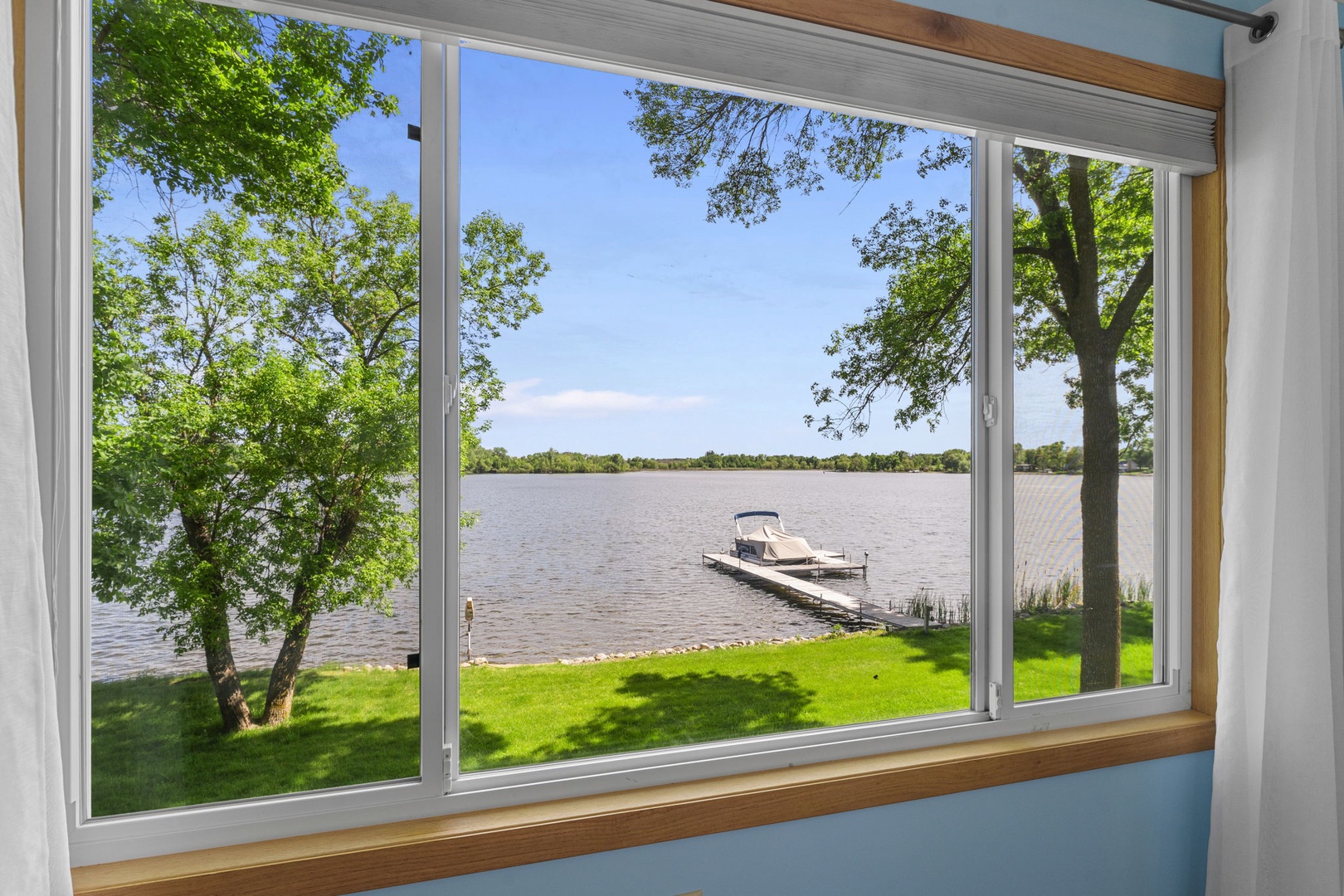 Tranquil lakefront setting with private dock and lush green lawn, framed by mature trees along the shoreline.