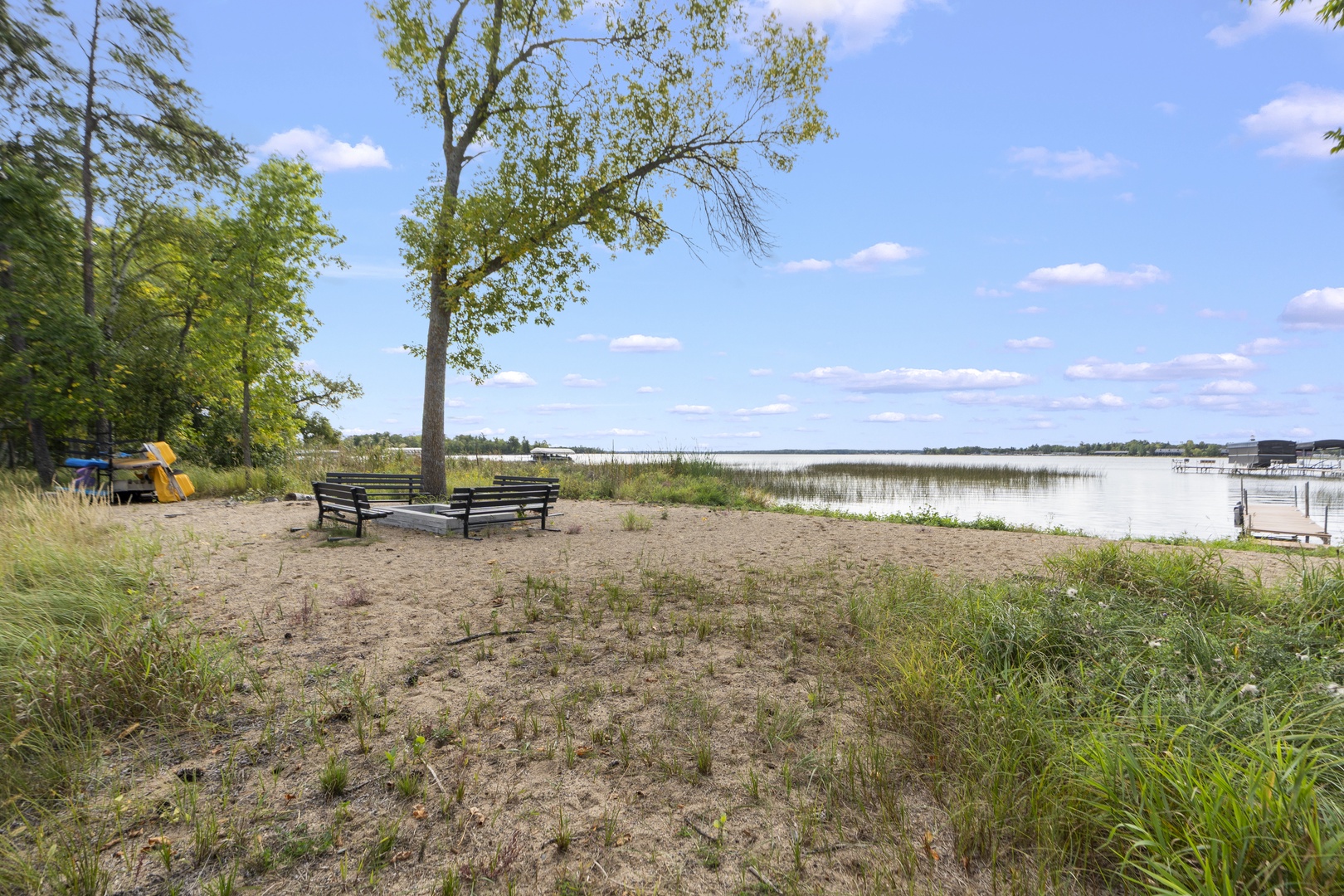 A peaceful lakeside setting with benches beneath shade trees and natural grasses, perfect for morning reflection or an afternoon of quiet relaxation by the water.