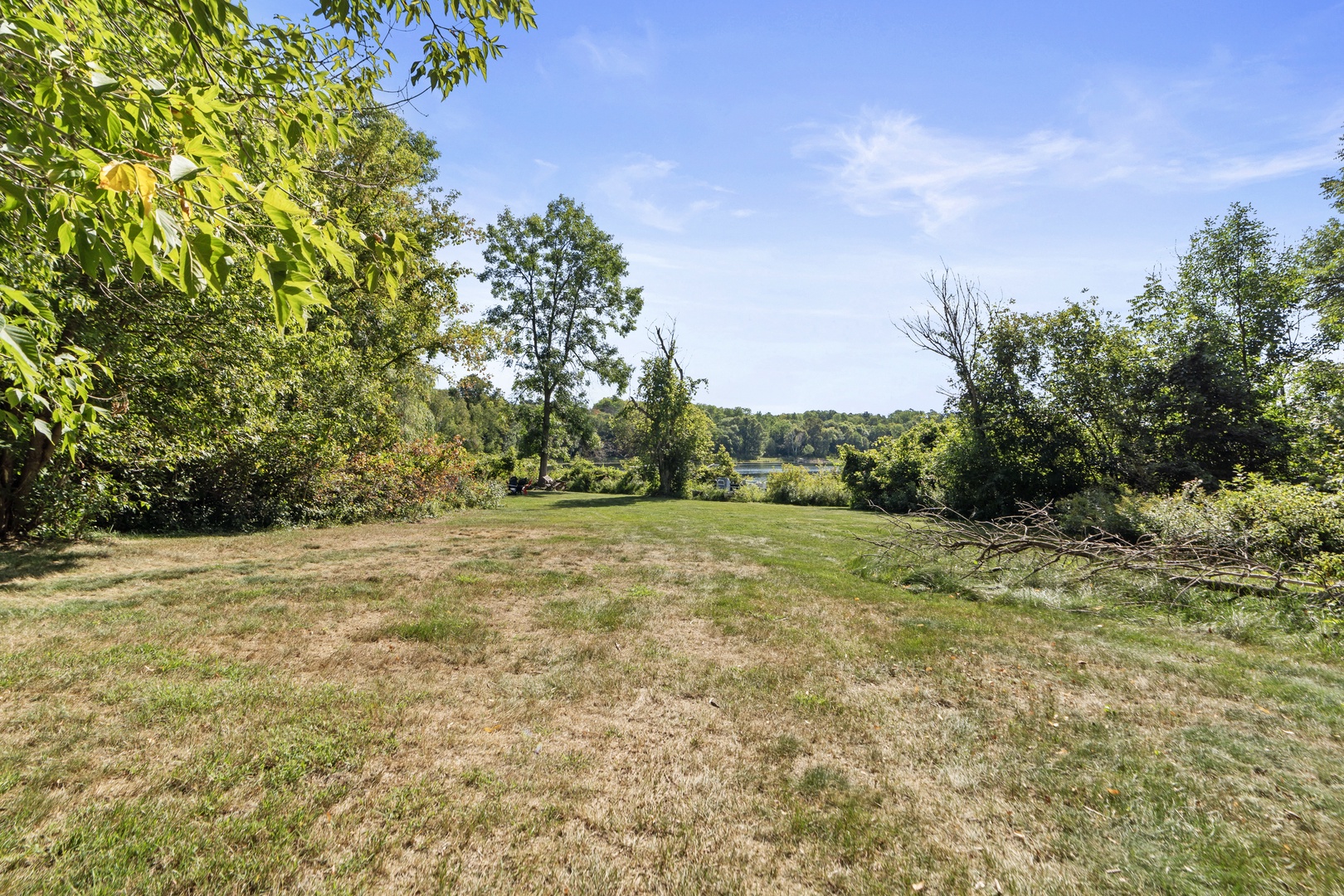 Spacious open grounds framed by mature trees and natural landscape, offering peaceful surroundings with glimpses of water beyond the greenery.