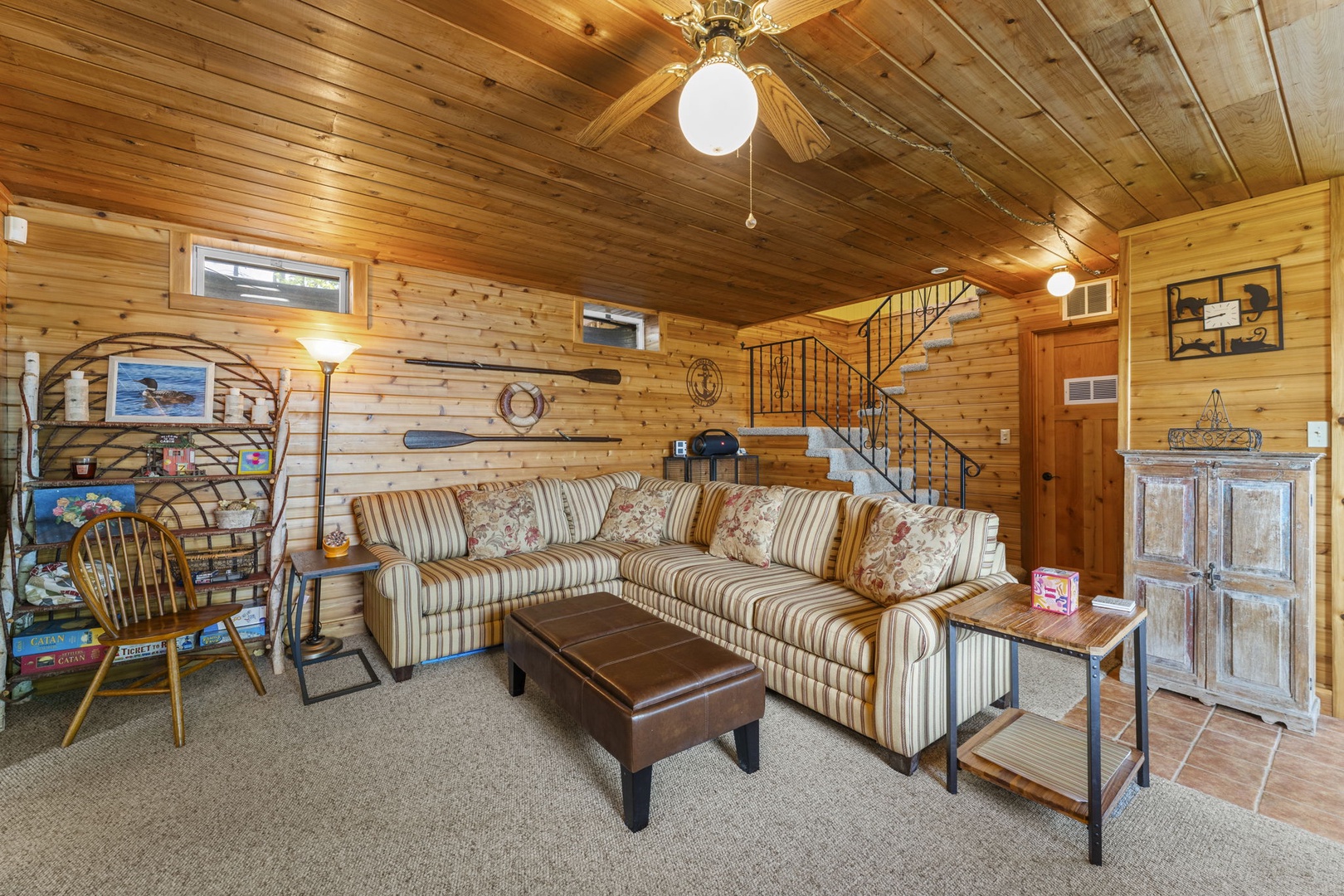 Sink into the plush striped sofa and unwind in this cozy cabin living room, where warm wood walls and charming nautical touches create your perfect retreat after a day of adventure.