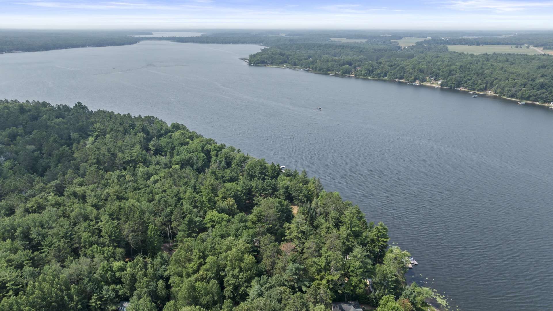 An aerial view captures the stunning lake setting surrounded by dense forest, with docks and tranquil waters stretching into the distance under a clear blue sky.