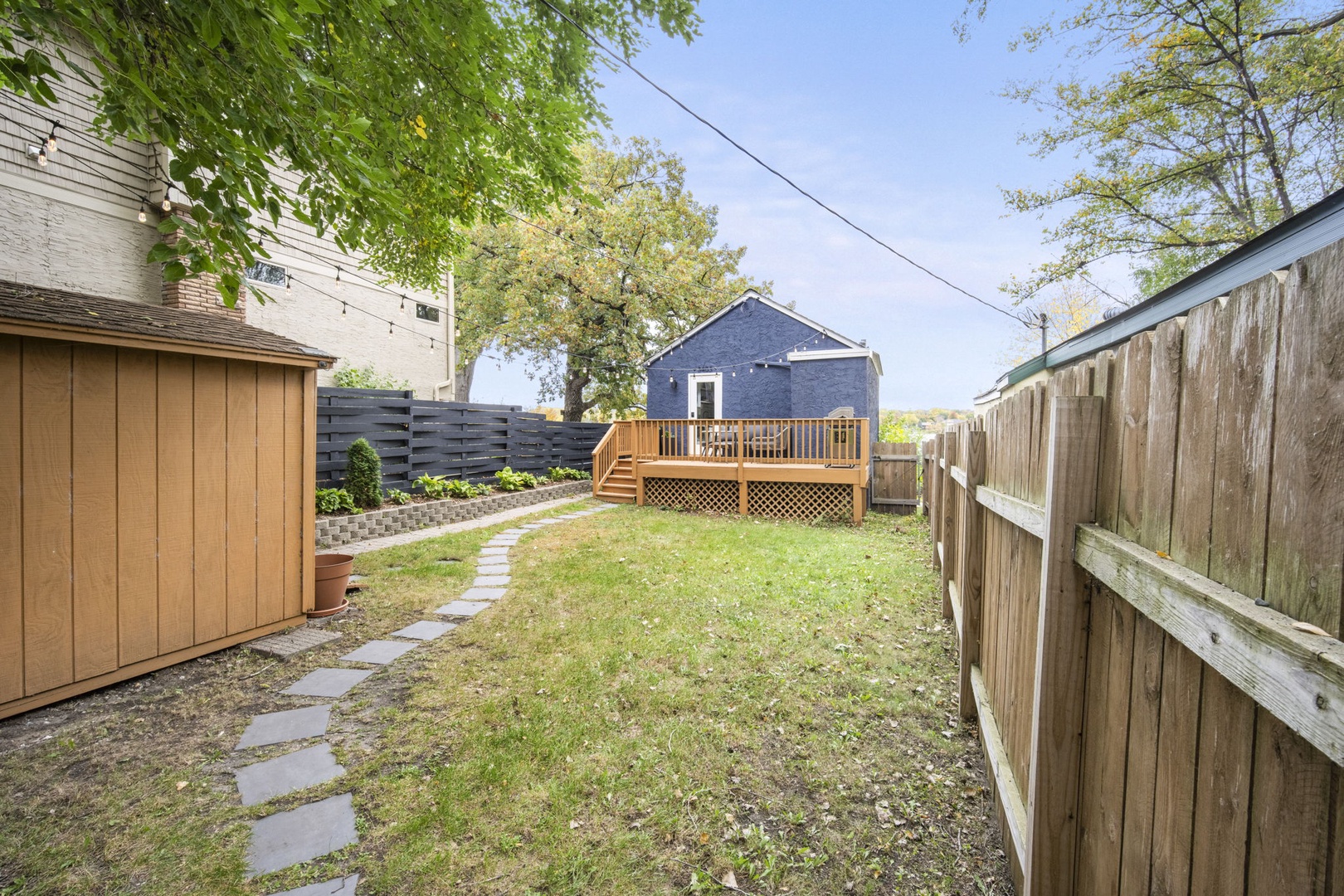 A private backyard oasis featuring a lawn bordered by mature trees and a charming wooden deck where you can unwind outdoors.