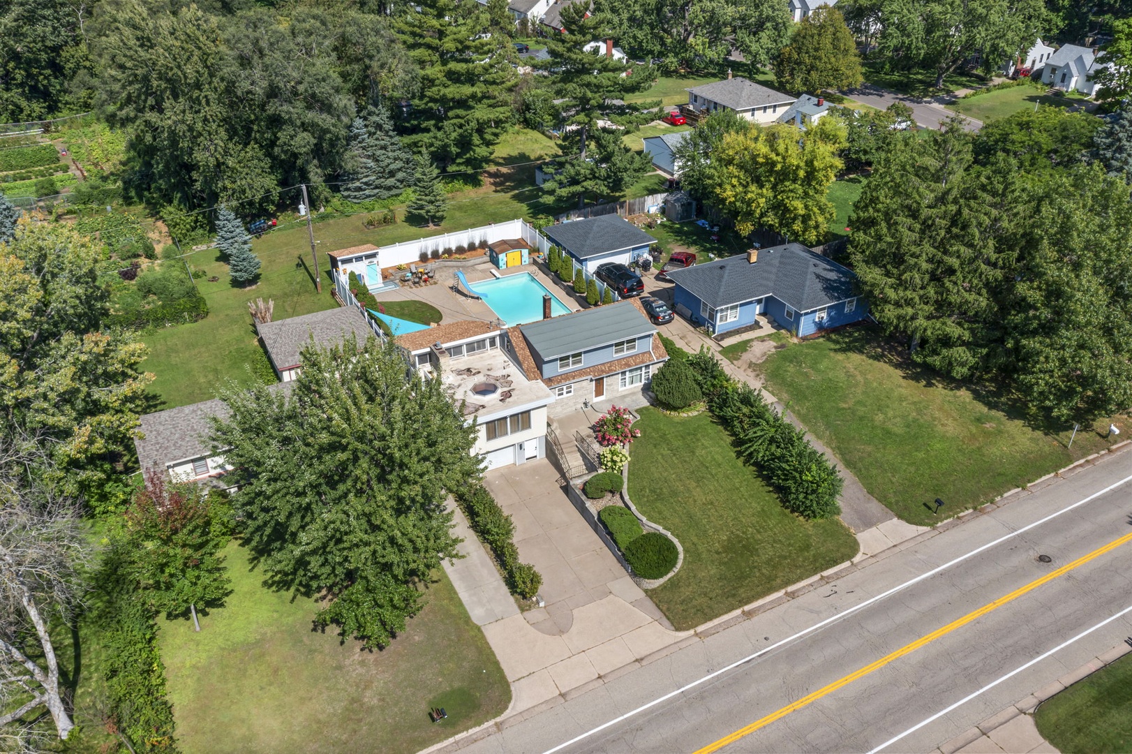 Aerial view of a spacious residential property featuring landscaped grounds, and mature trees in a quiet neighborhood setting.