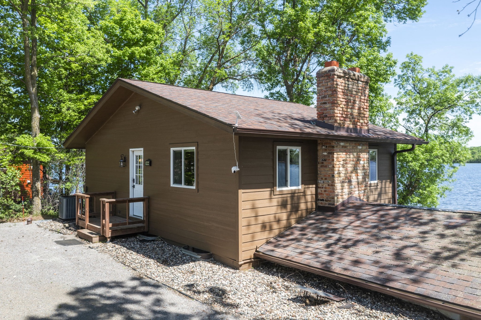 Cozy lakeside cottage with red-brick chimney nestled in lush greenery, steps from the water's edge—a peaceful retreat for your getaway.