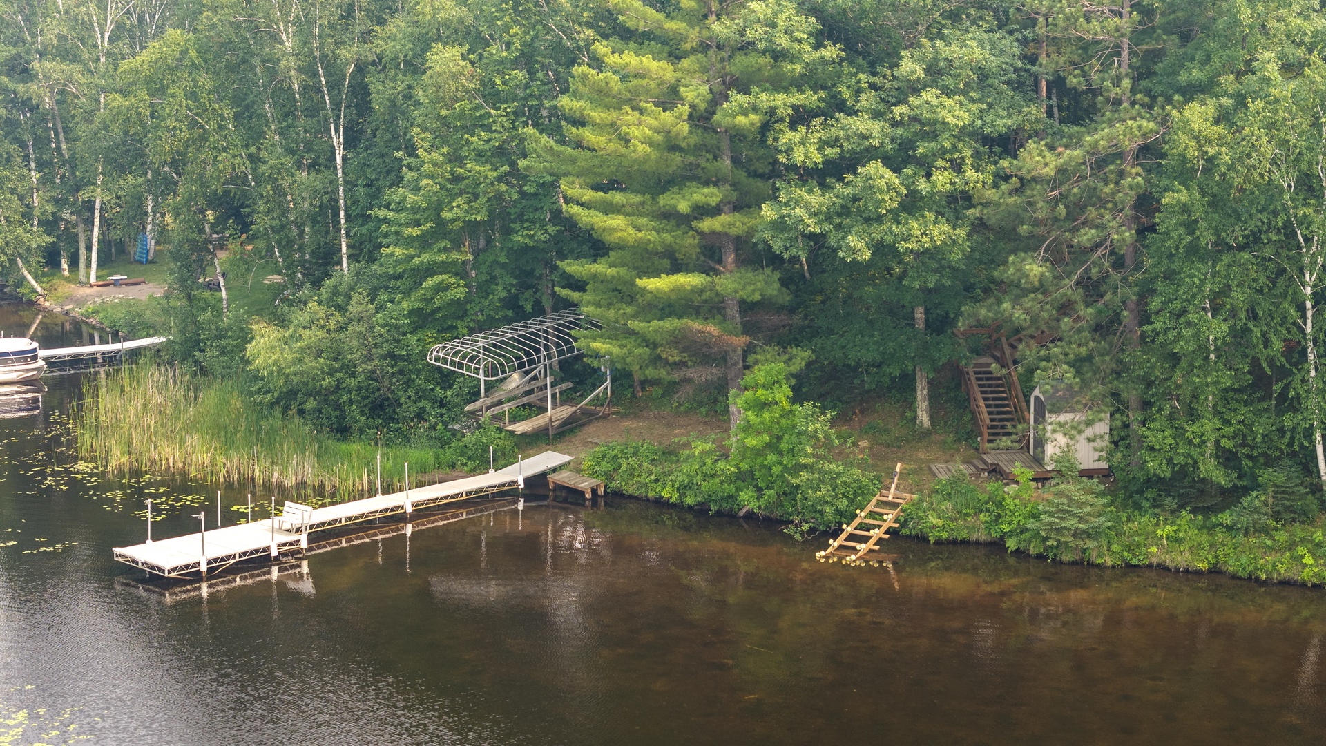 A peaceful lakefront property nestled among towering pines with private dock, swimming area, and wooded pathways winding through the natural landscape.