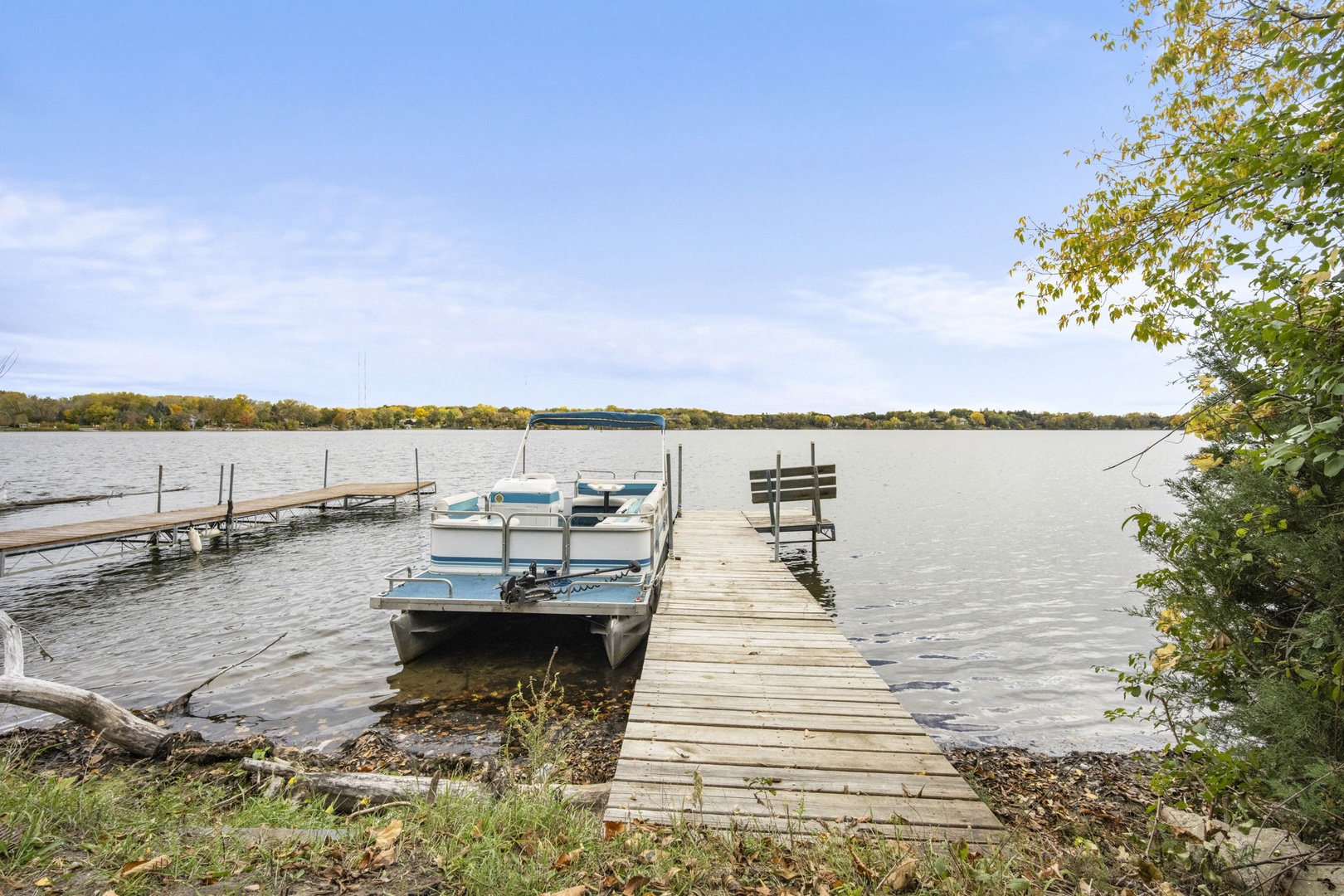 A private dock extends into calm lake waters. Surrounded by trees showing early autumn color, this peaceful waterfront invites leisurely afternoons by the shore.