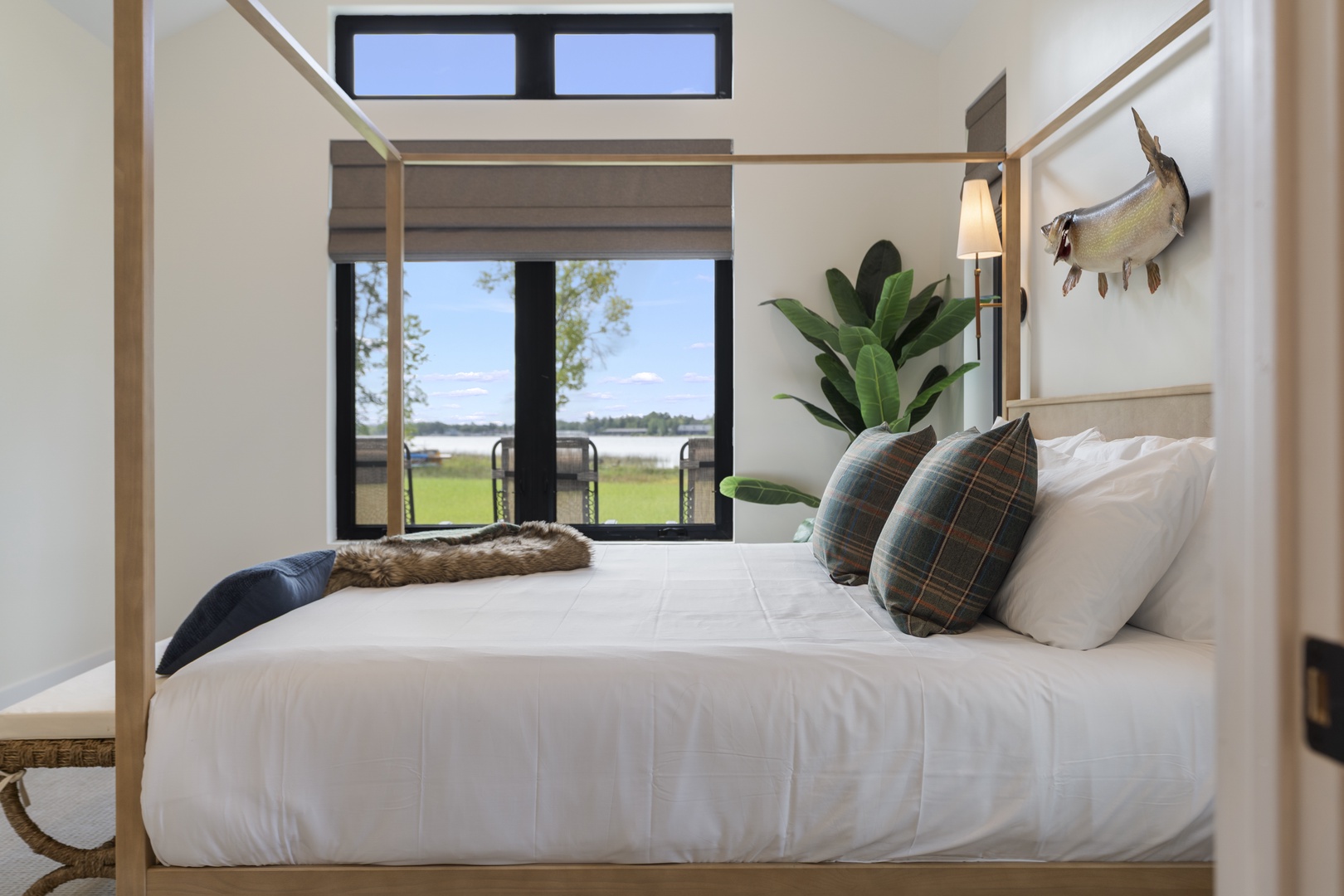 Sink into crisp white linens on your four-poster bed while gazing out at serene waterfront views framed by large glass doors. The soft bedside glow and natural decor invite your complete relaxation.