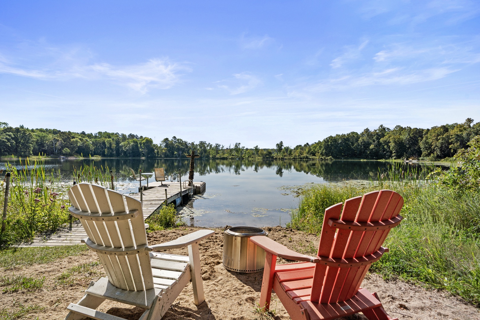 Private lakeside escape with a dock stretching out to calm waters, framed by lush forest and framed by colorful Adirondack chairs.