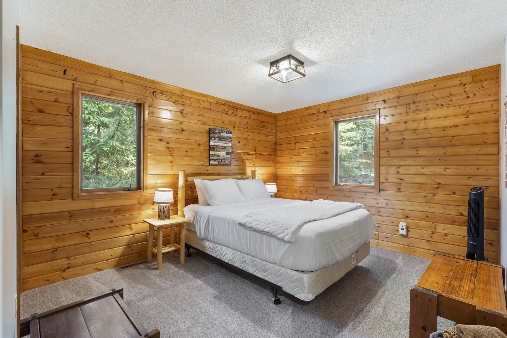 Drift off in your cozy bedroom wrapped in warm knotty pine, where morning light filters through windows framing peaceful forest views. Simple comforts meet natural charm.