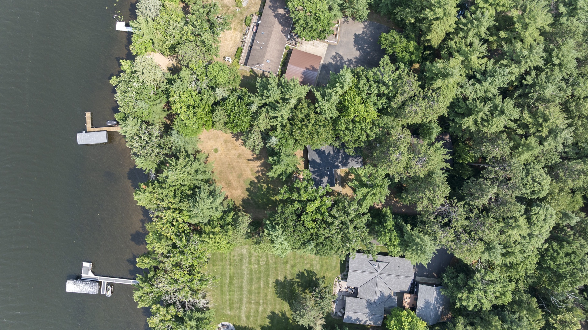 Aerial view of a secluded lakeside property surrounded by lush forest, featuring private docks and access to tranquil waters.