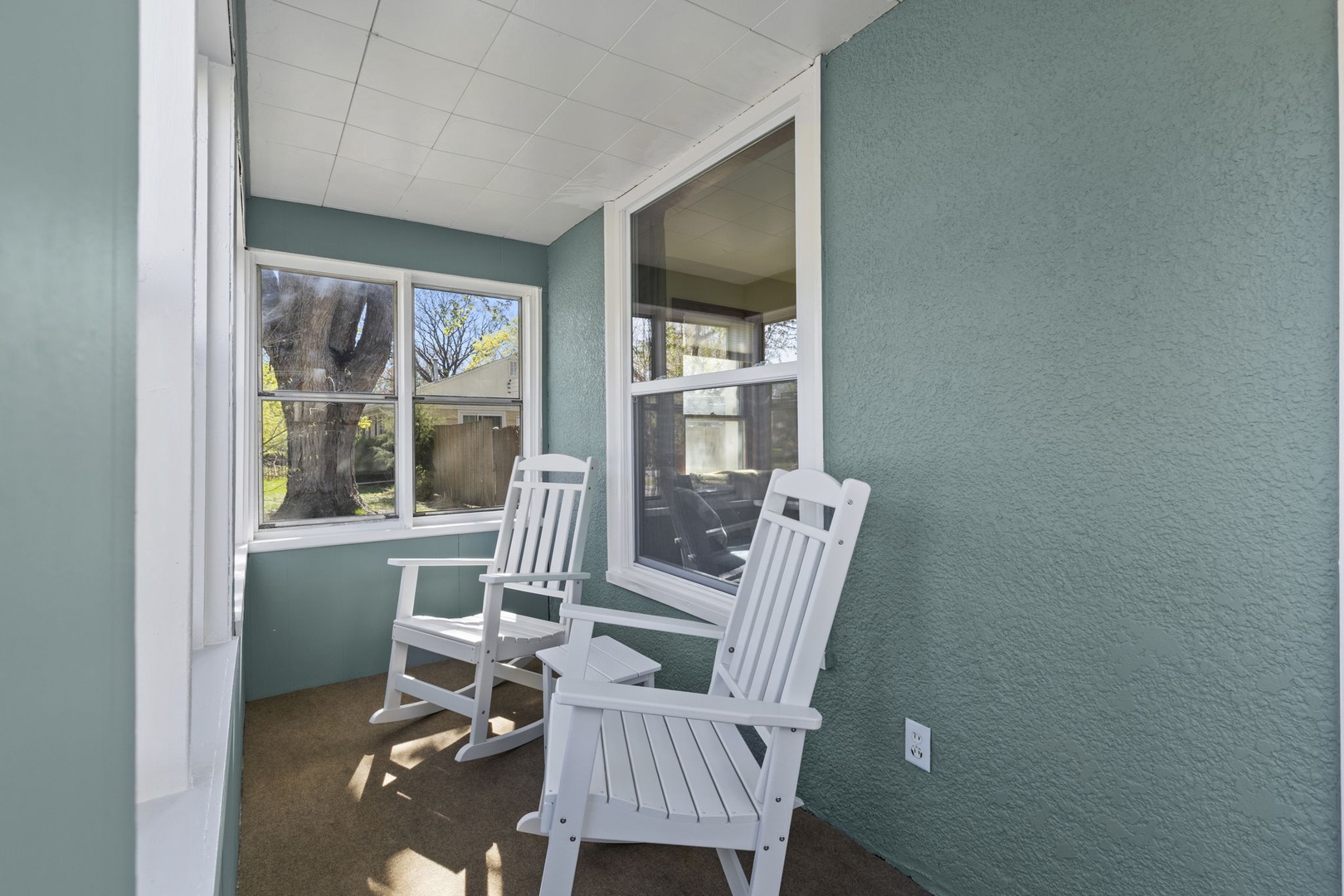 Bright enclosed porch with two white rocking chairs and wrap-around windows — a sun-soaked bonus space to relax any time of year.