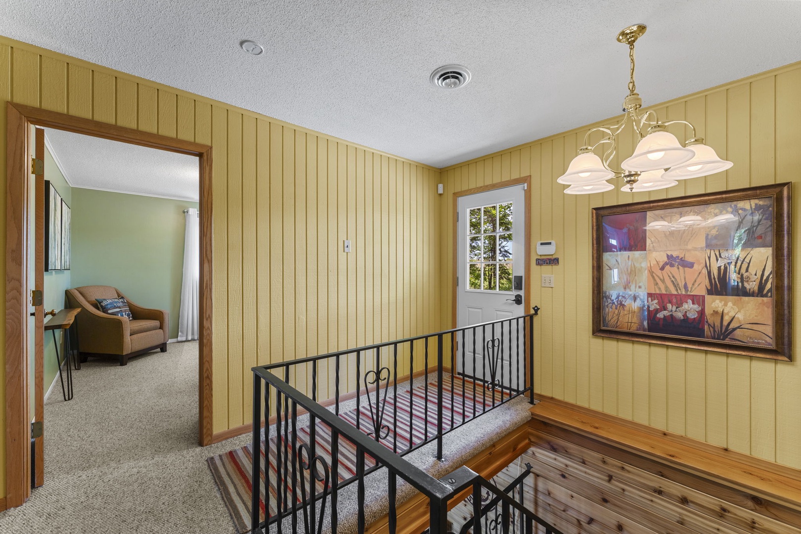 Warm wood paneling and cheerful artwork greet you at the top of the stairs, with natural light streaming through the door to guide your way inside.