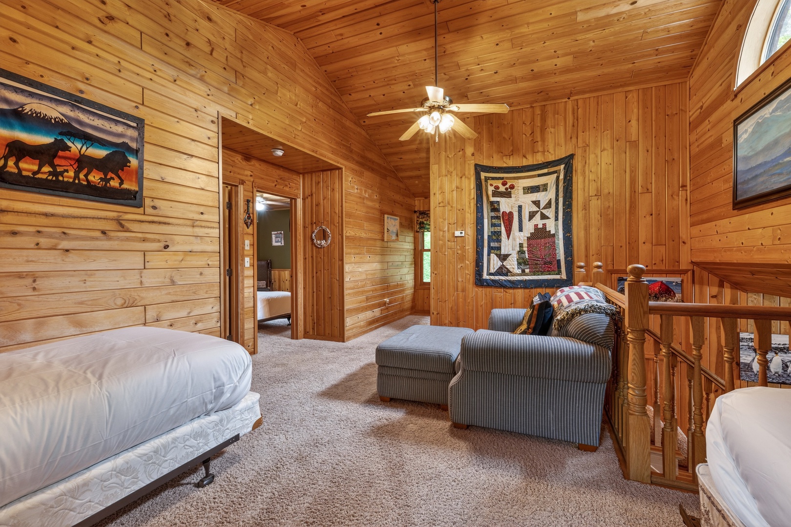 Convenient sleeping loft with two twin beds, soft carpeting underfoot, a cozy ceiling fan, and charming rustic artwork. Your perfect mountain retreat awaits.