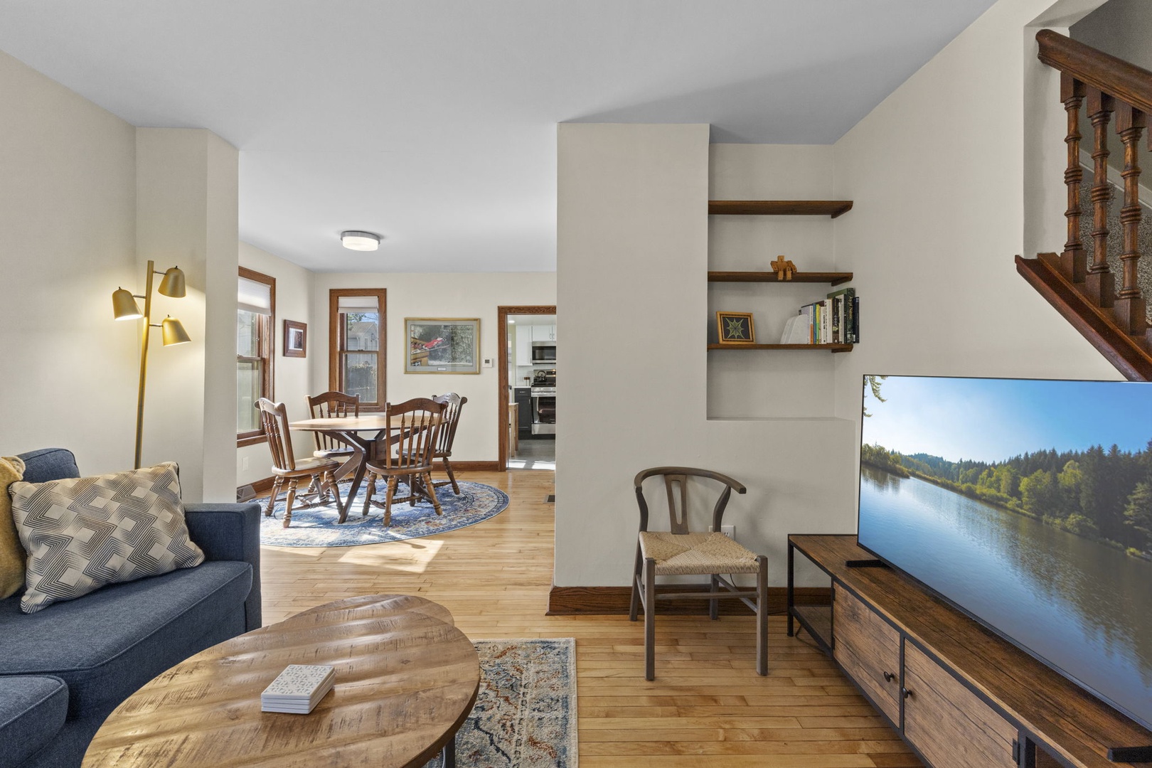 Open-concept living and dining area with smart TV, built-in wood shelving, and original hardwood floors — bright, airy, and connected to the kitchen.