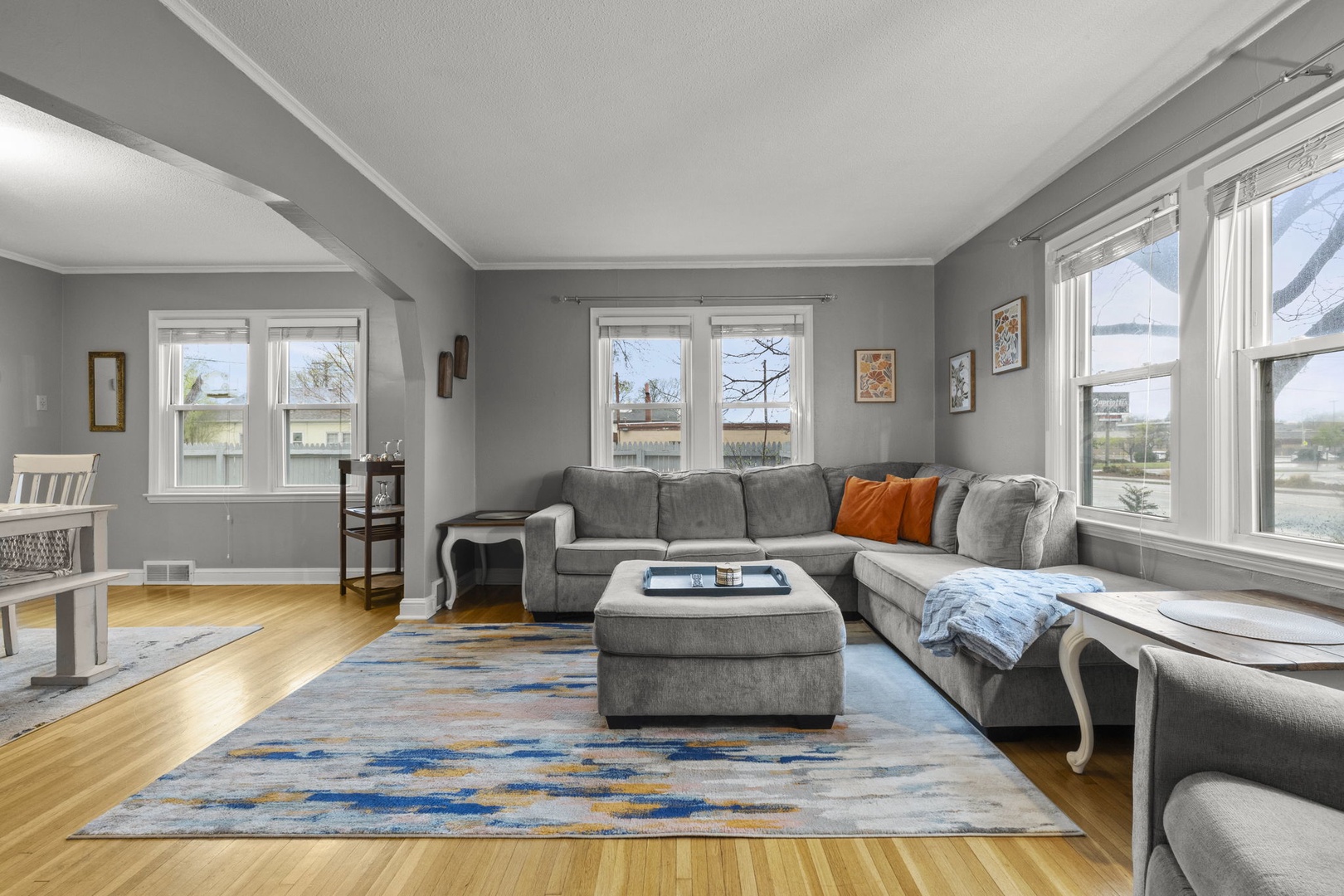 Stretch out on the plush sectional and soak in natural light from every angle. Your peaceful retreat features warm hardwood floors, soothing grey tones, and generous windows framing the open landscape beyond.