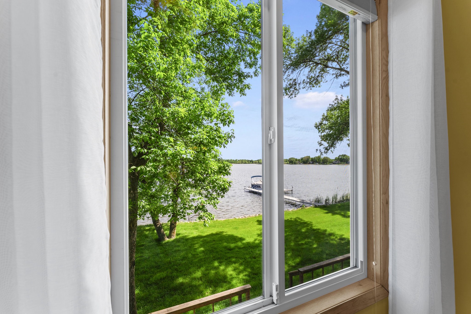 Gaze out at the shimmering lake just steps from your window, where lush green lawn and swaying trees frame a perfect waterfront escape for your morning coffee.