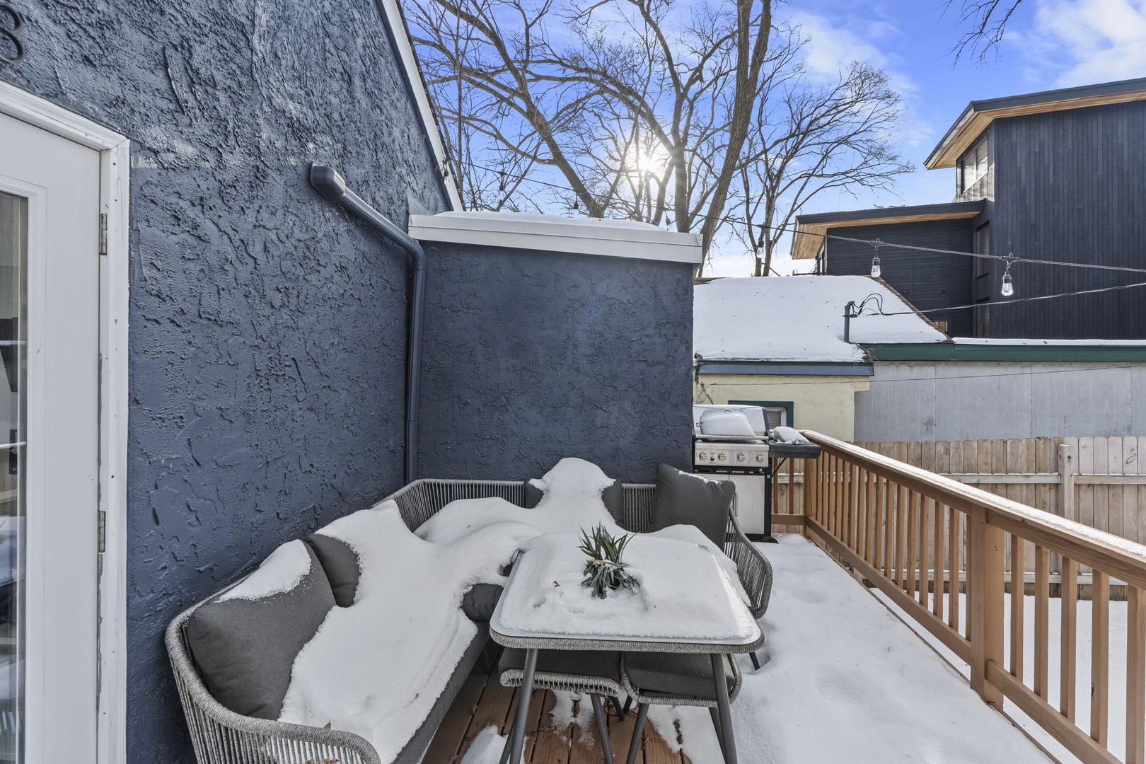 Snow-dusted outdoor patio with modern dining furniture and BBQ setup in a quiet residential neighborhood during winter season.