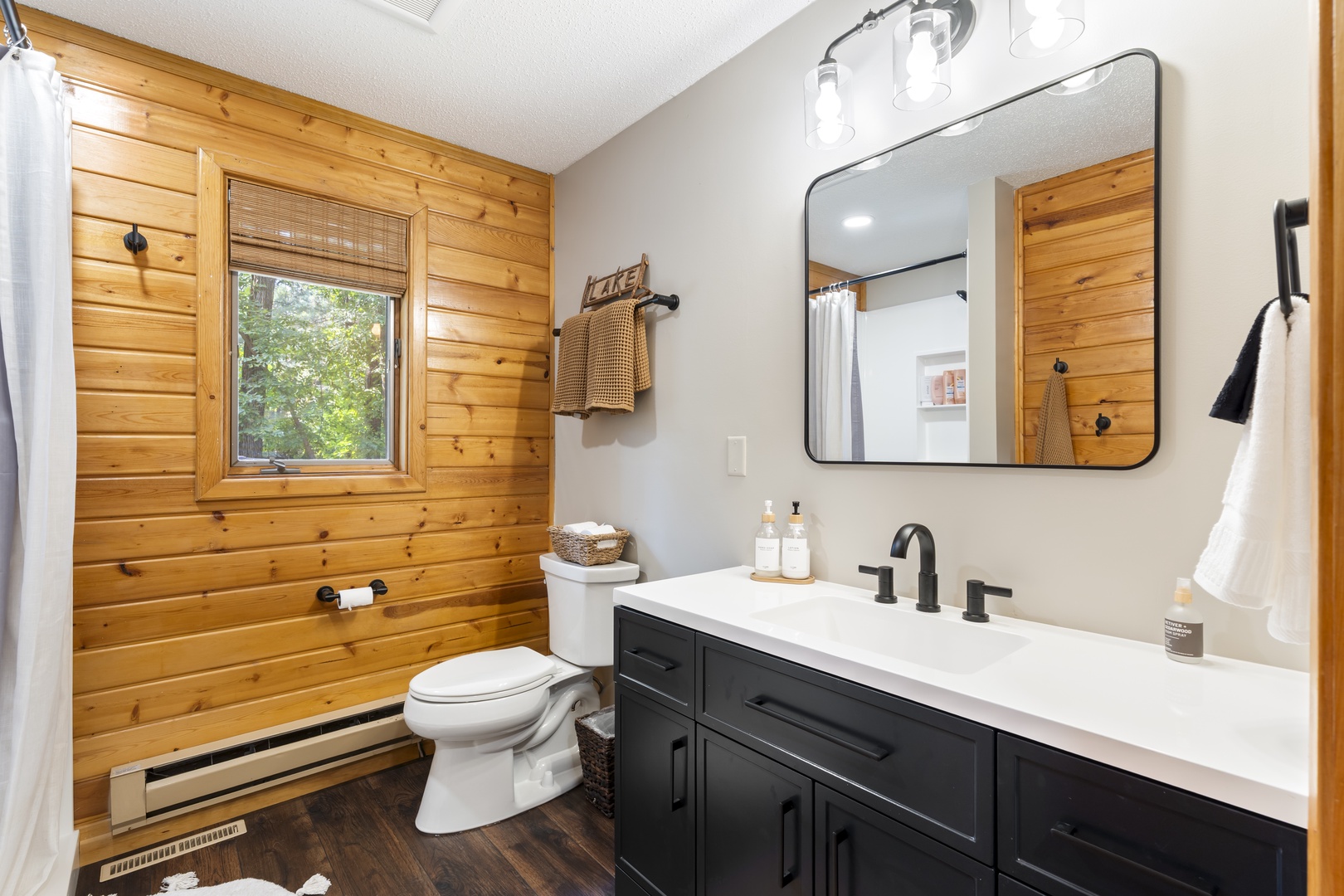 Freshen up in your tastefully designed bathroom with warm wood accents, a sleek vanity, and natural light streaming through the window. Crisp white towels and modern fixtures complete this inviting space.