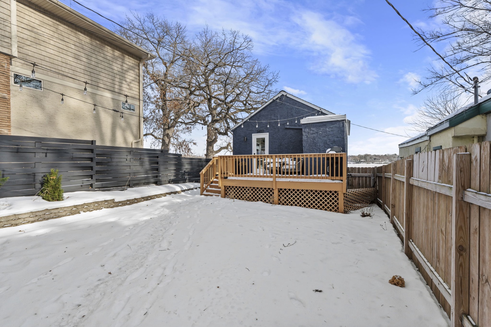 Snow-covered backyard with wooden deck offering peaceful winter views in a quiet residential setting.