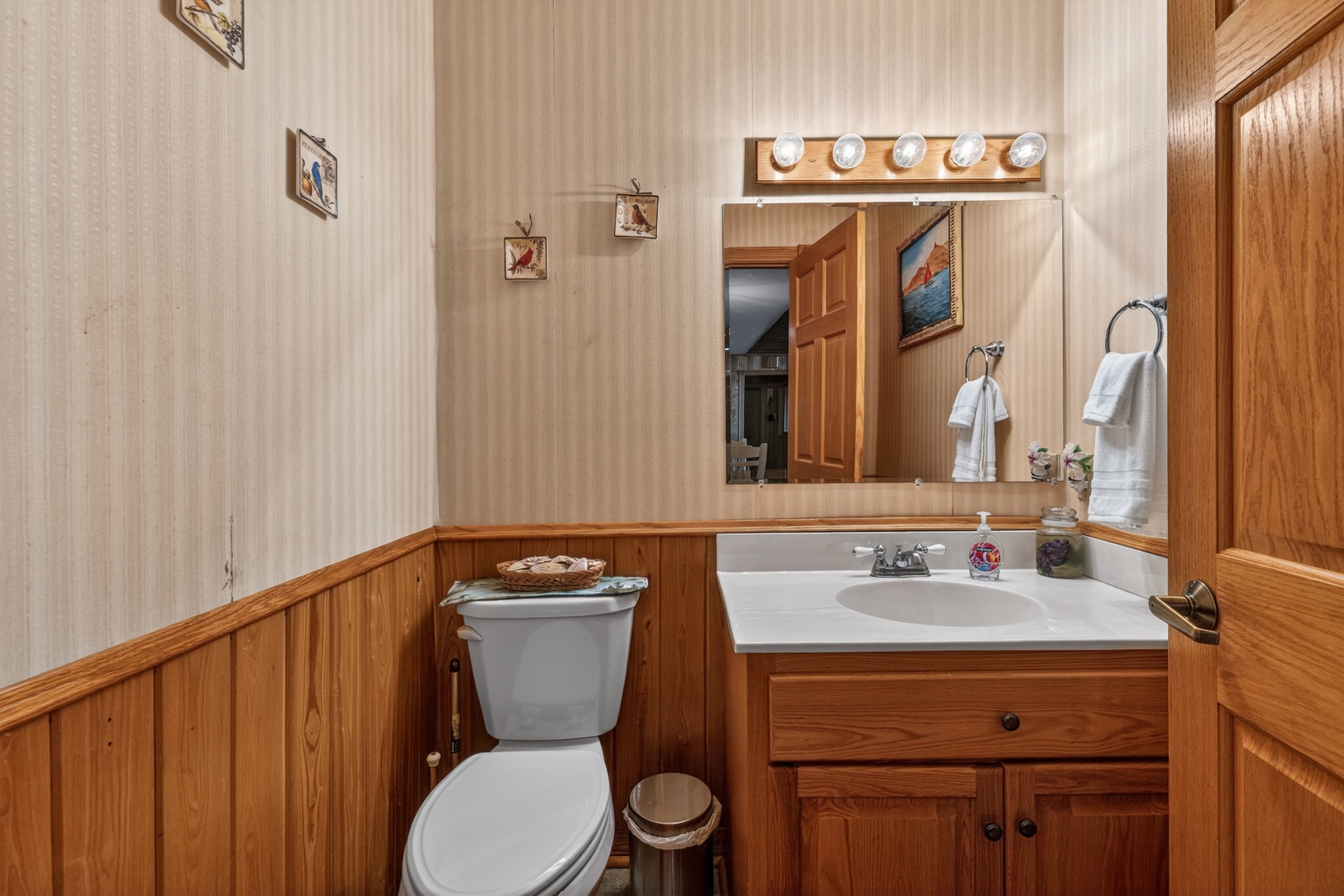 The main floor half bathroom features warm wood accents, a well-lit vanity mirror, and fresh towels ready for your arrival—homey and comfortable.