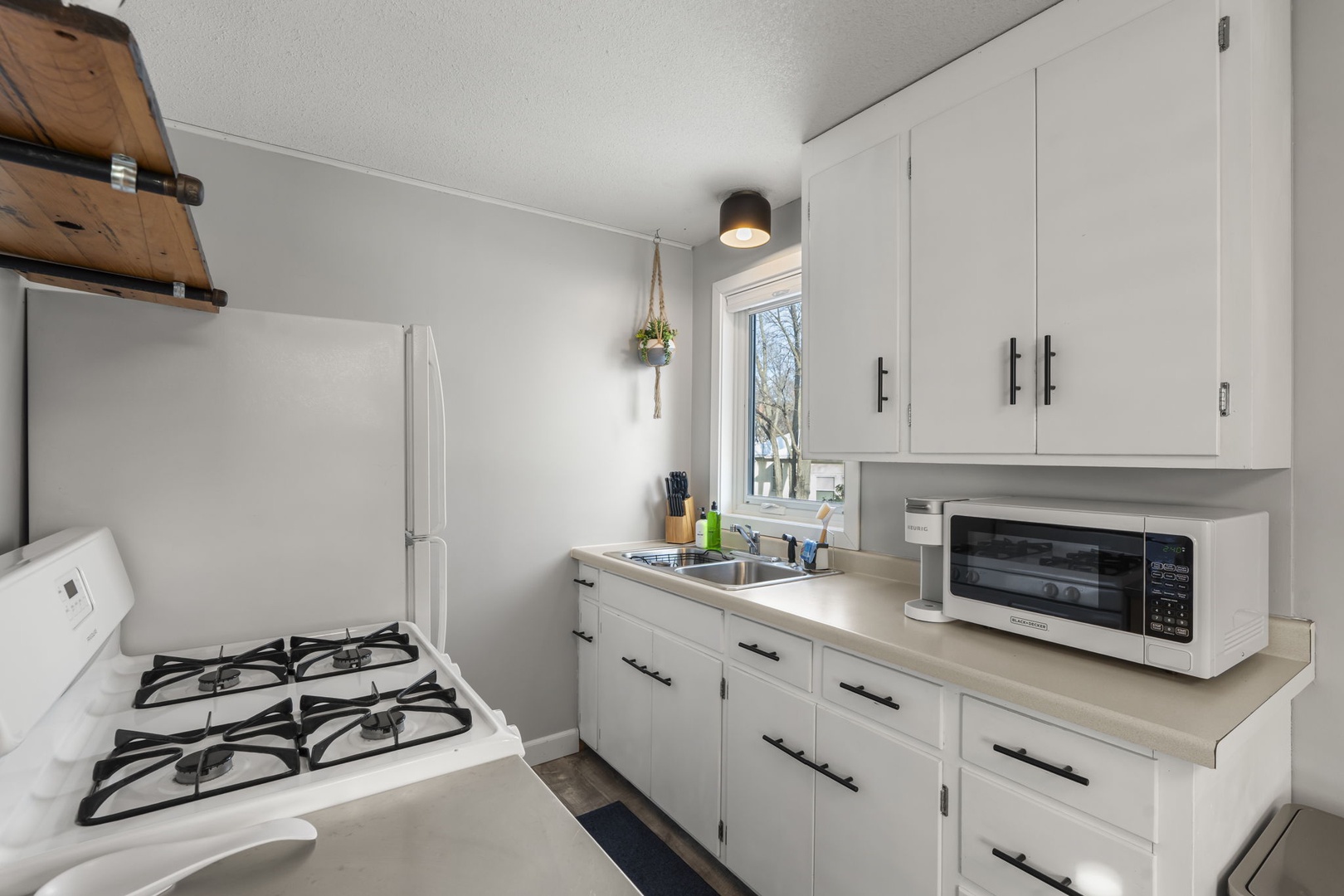 Your fully equipped kitchen features everything you need to prepare meals, with bright white cabinets, modern appliances, and natural light streaming through the window.