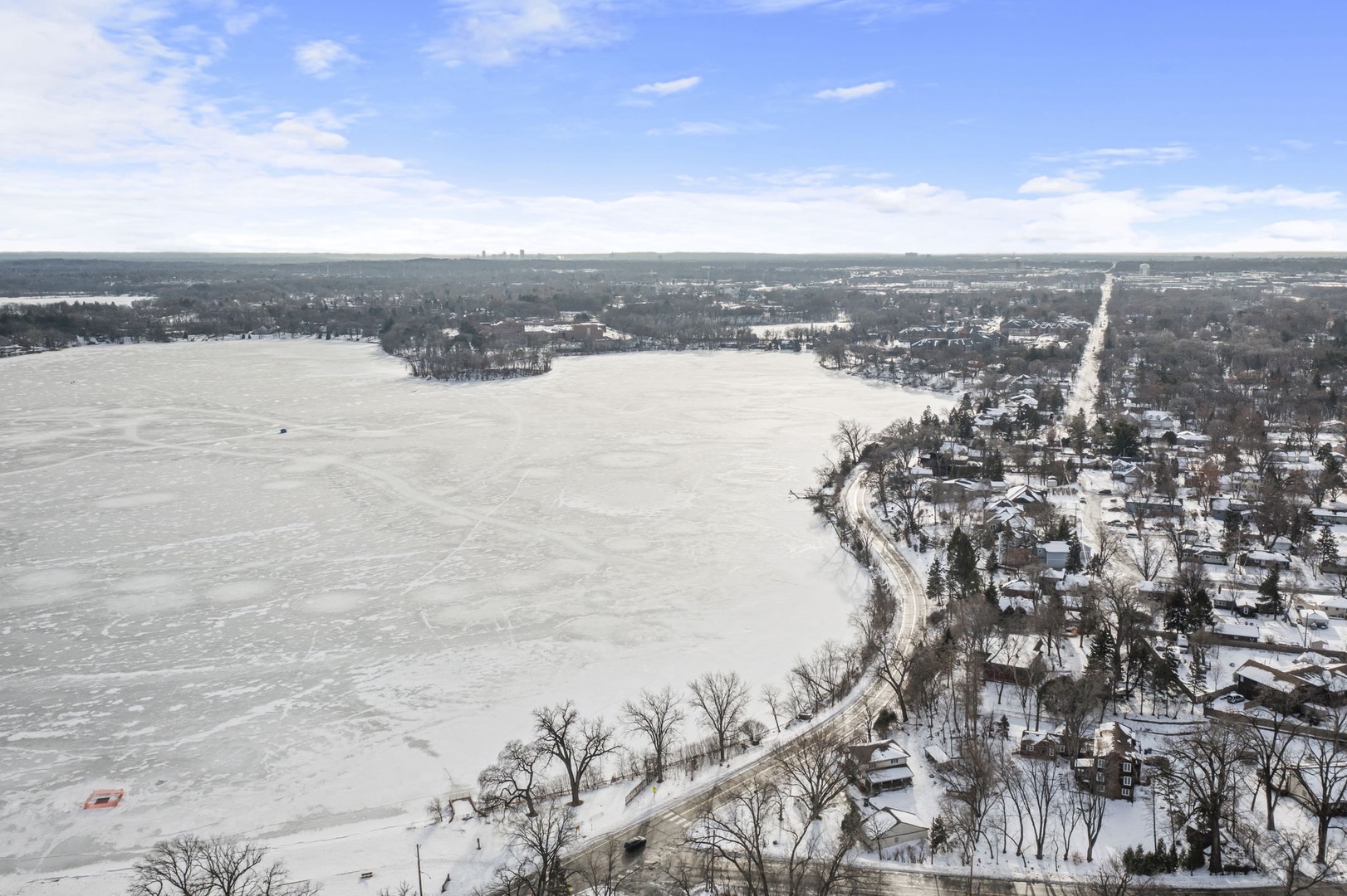 Aerial winter view showcasing a frozen lake surrounded by snow-covered residential neighborhoods and tree-lined streets.