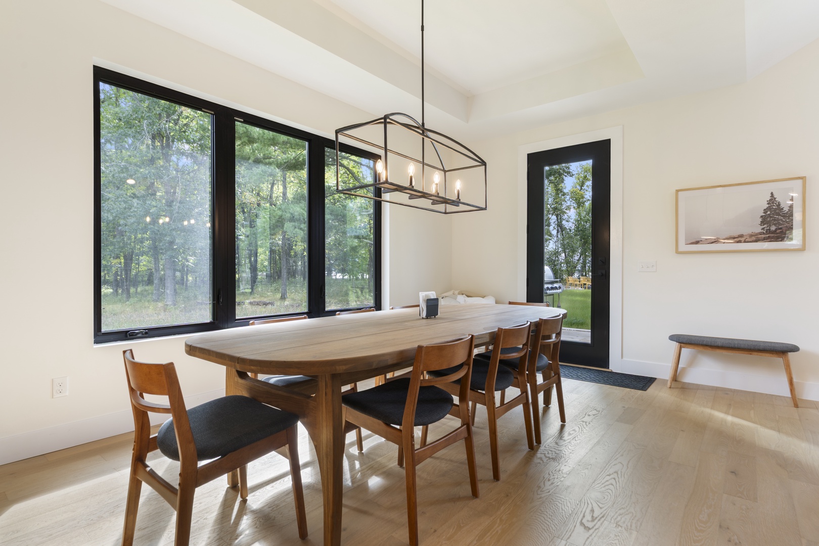 Gather around the warm wood dining table as natural light pours through stunning floor-to-ceiling windows, offering peaceful forest views that make every meal feel like a retreat.