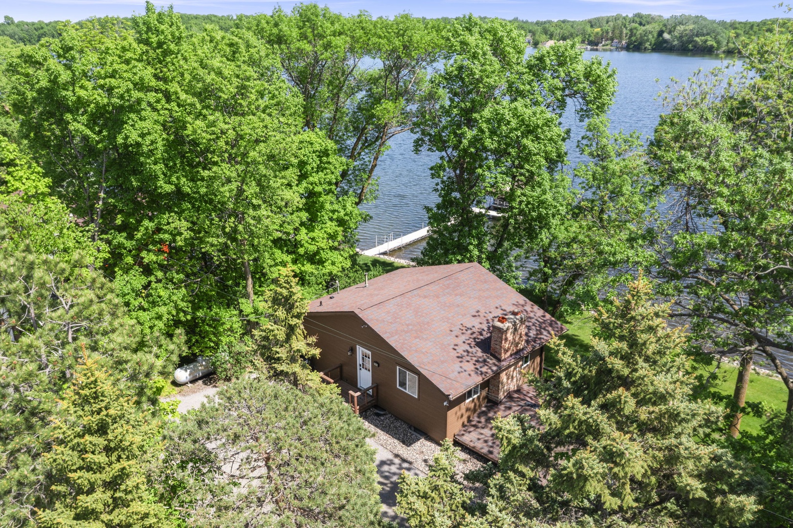 Aerial view of a lakefront vacation home nestled among lush trees, with private dock access and scenic waterfront surroundings.