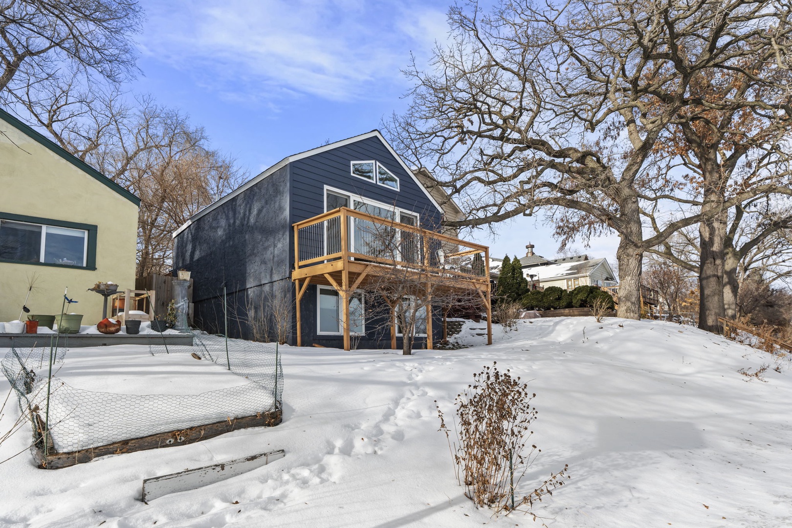 Charming winter retreat with deck surrounded by snow-covered grounds and mature trees.