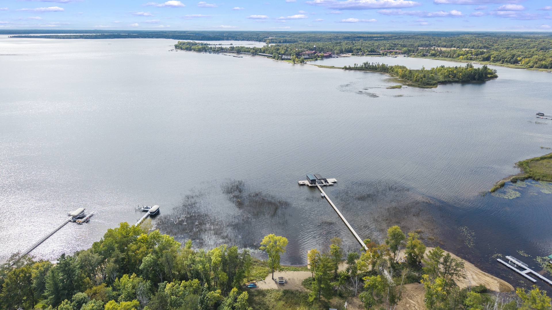 An aerial view captures the property's prime lakefront location, with private dock access stretching out over calm waters. Islands dot the lake, and lush greenery frames the shoreline, showcasing the peaceful natural setting.