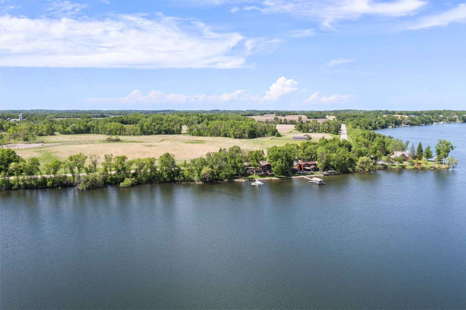 Aerial view of a waterfront property nestled along a serene lake, surrounded by lush greenery and open fields.