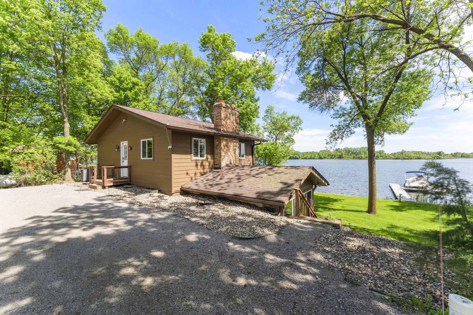 Lakefront property nestled among mature trees with direct water access and spacious gravel parking. The setting offers serene views and a private dock for waterfront activities.