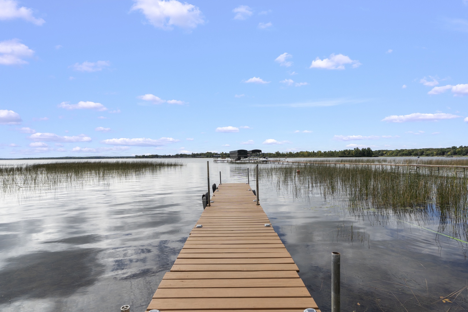 A private dock extends into tranquil lake waters, framed by natural reeds and expansive sky—perfect for peaceful waterside moments and easy access to the lake.