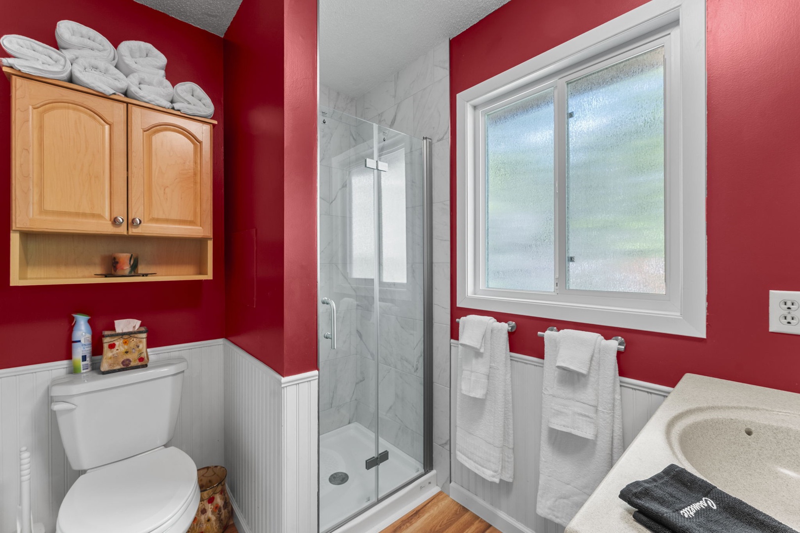 Step into your private bathroom with bold red walls, a refreshing walk-in shower, and fresh towels waiting. The space feels clean, bright, and thoughtfully stocked for your comfort.
