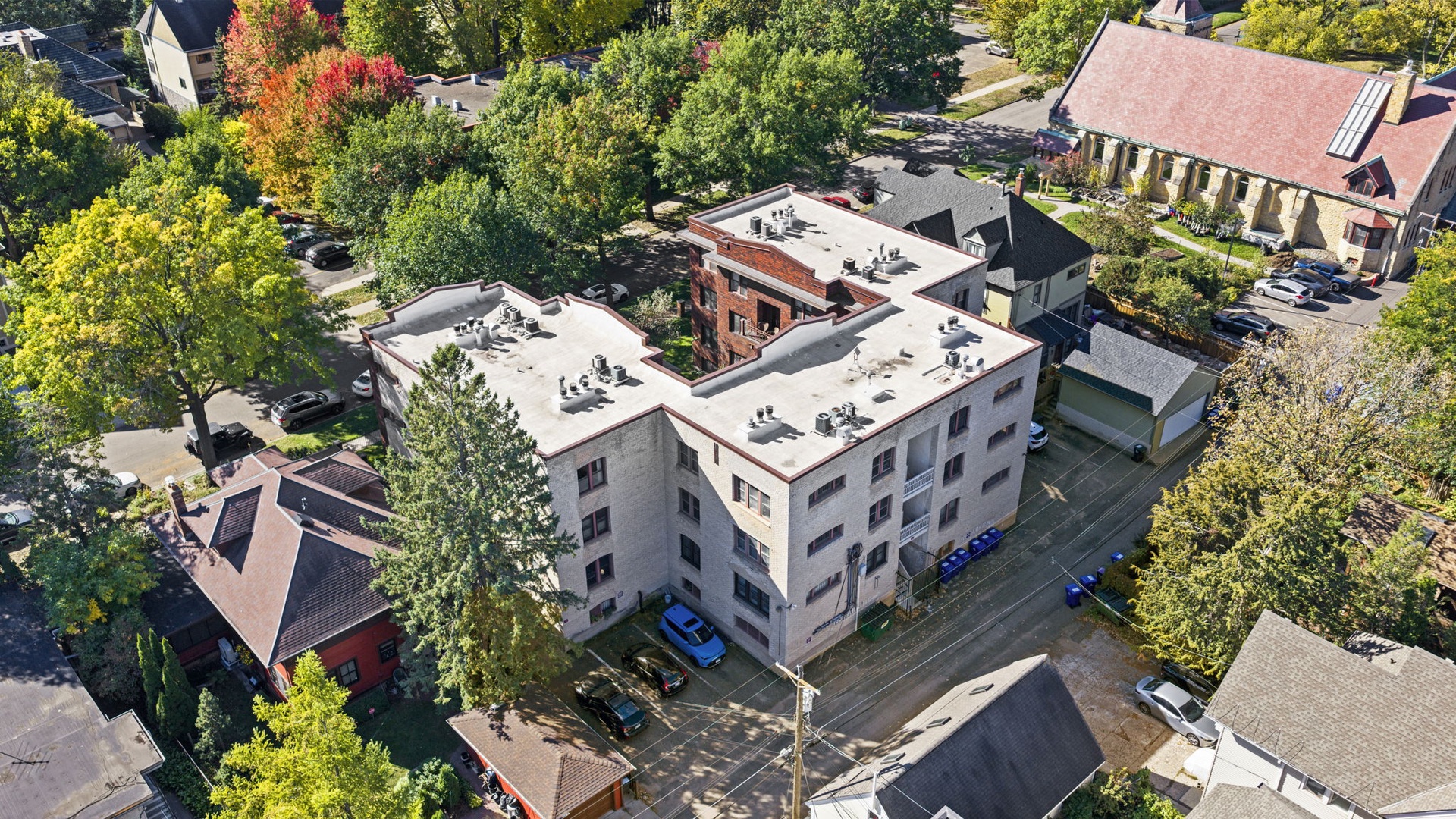 Aerial view of the property situated in a peaceful residential neighborhood with mature trees and convenient parking. The multi-story building is surrounded by a quiet, tree-lined area with nearby local amenities.