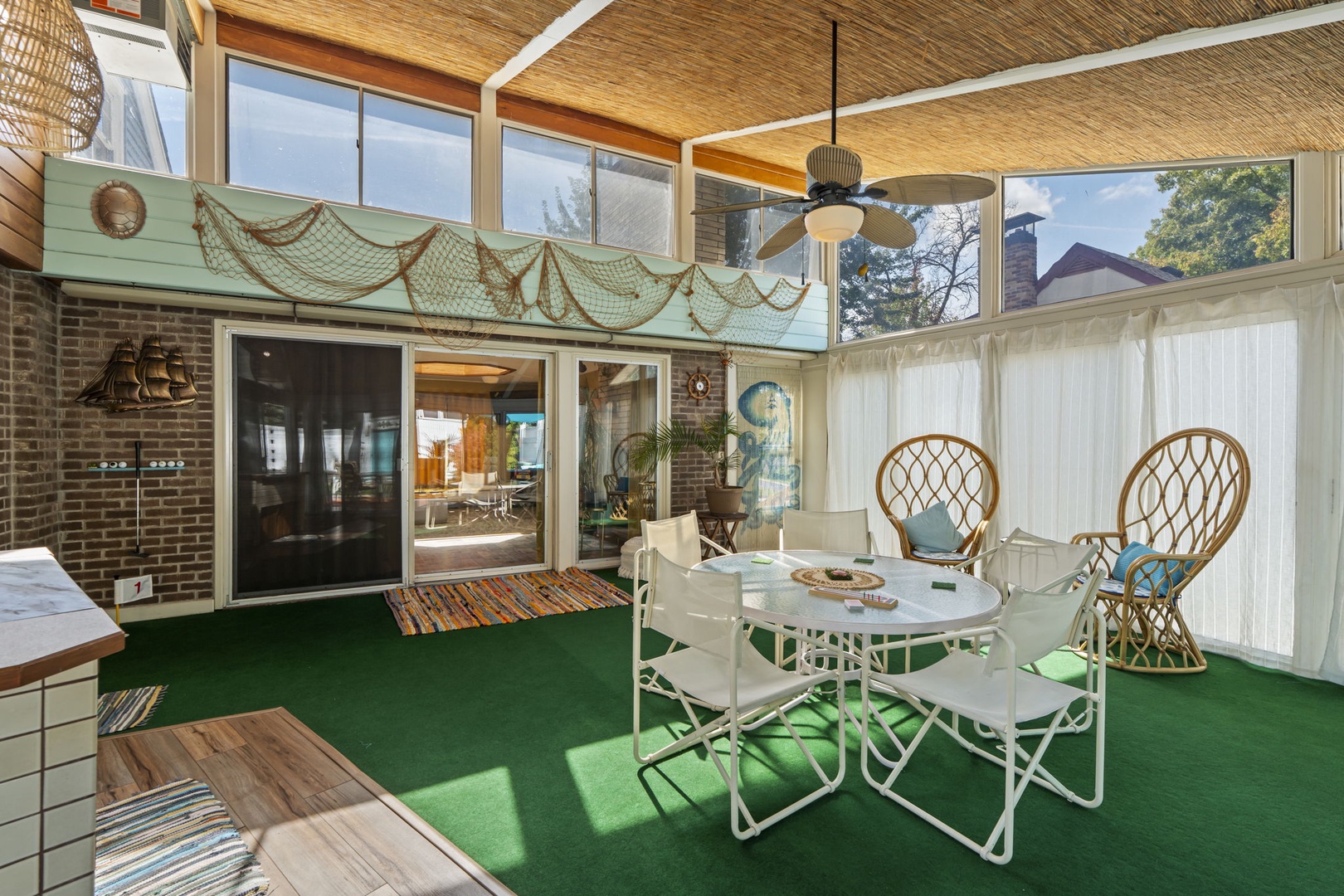 Relax in your bright enclosed patio with nautical charm, featuring unique wicker chairs and ceiling fan for comfortable dining year-round.