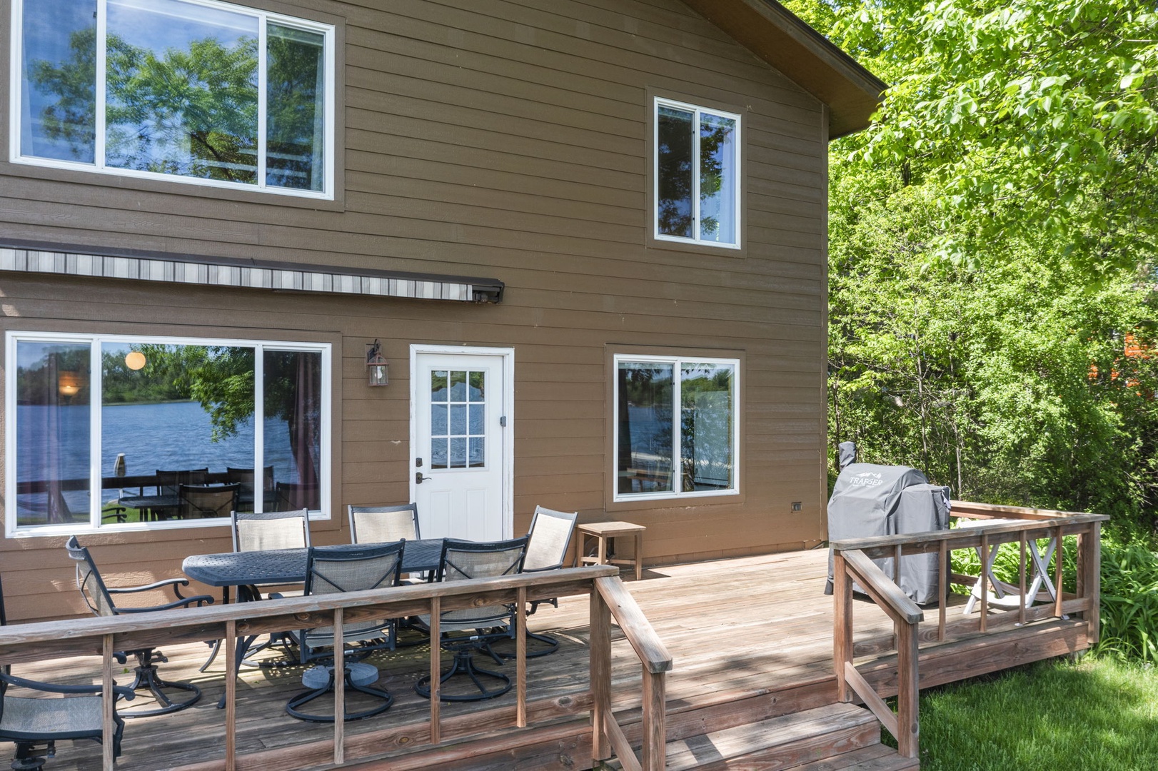 The spacious back deck overlooks lush greenery, featuring dining furniture and a grill—perfect for your outdoor meals and peaceful relaxation surrounded by nature.