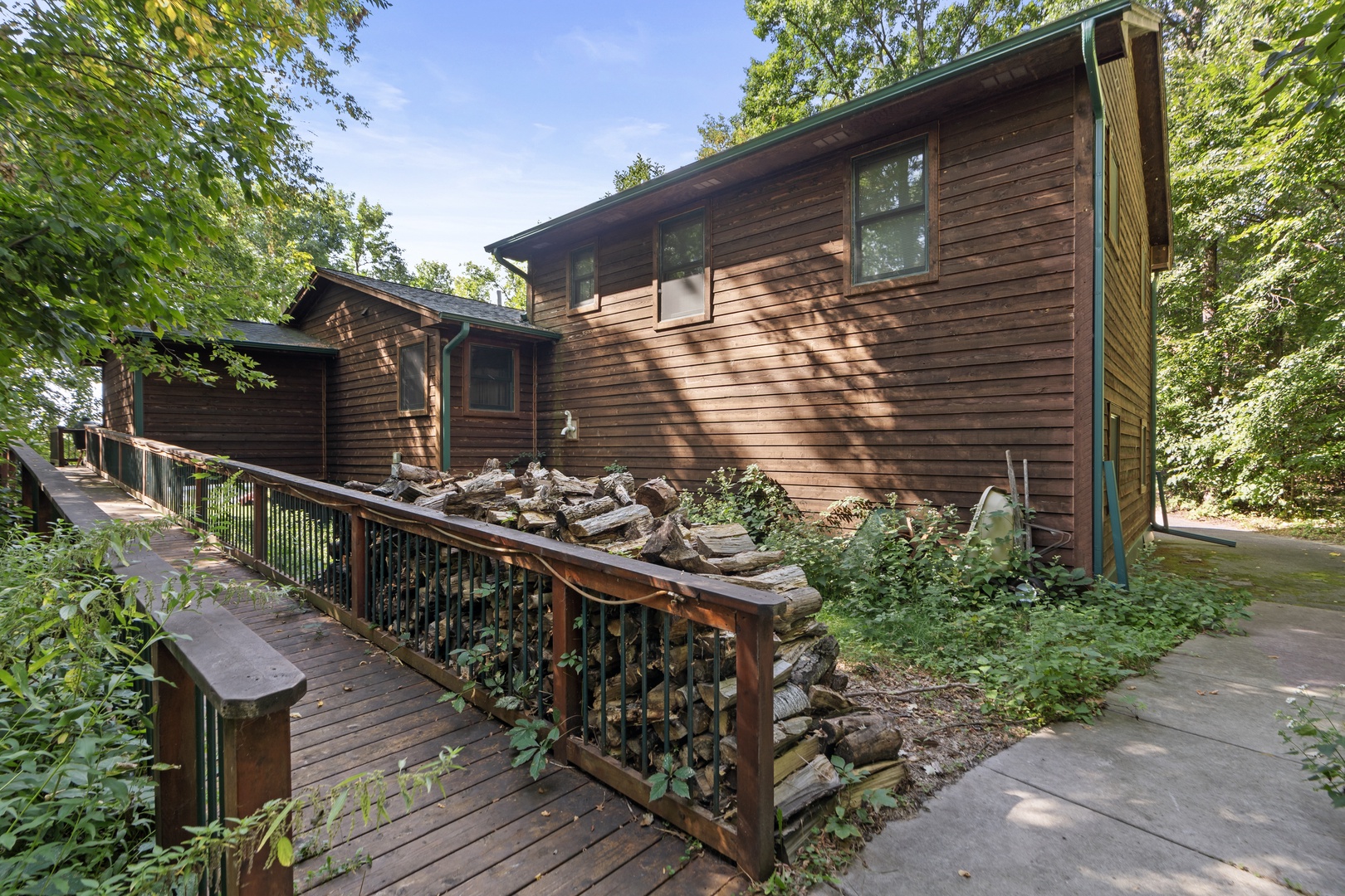 Rustic wood-sided cabin nestled among mature trees with a private deck and garden area at the entrance.