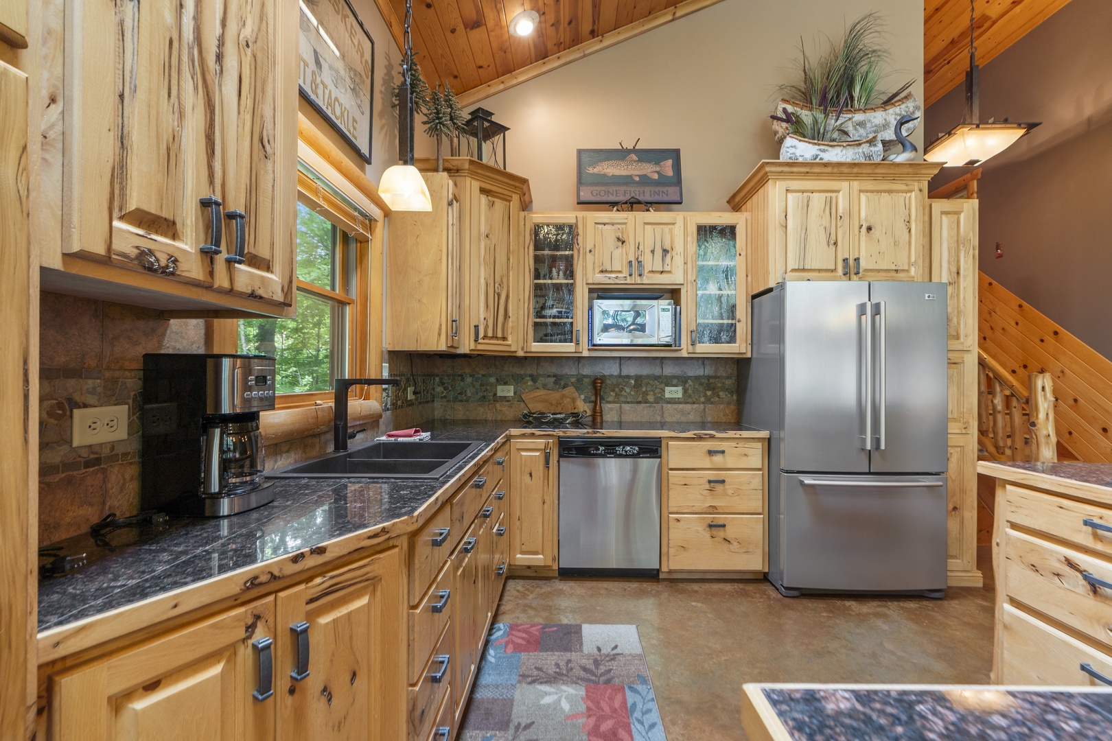 Your fully-equipped kitchen blends rustic charm with modern convenience, featuring custom wood cabinetry, gleaming granite counters, and stainless appliances beneath warm wood-paneled ceilings and natural light.