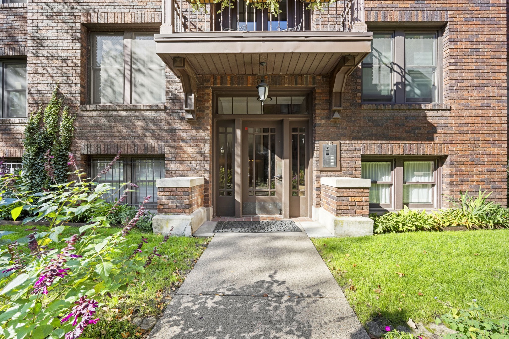 A charming brick building welcomes you with a landscaped entrance, featuring vibrant flowers and greenery that frame the pathway to your retreat.
