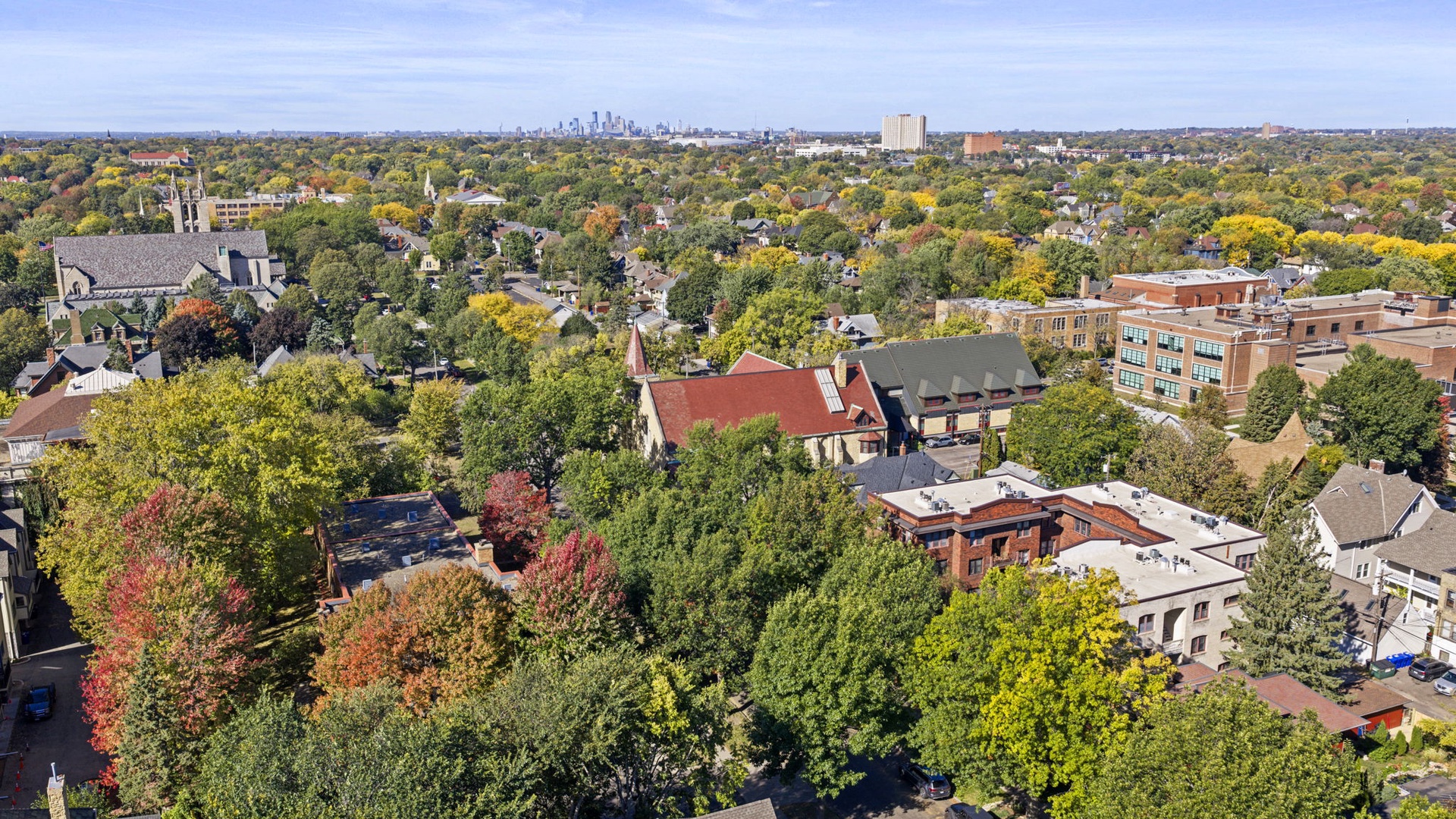 Aerial view of a tree-lined neighborhood with fall foliage and distant city skyline, showcasing the surrounding residential area.
